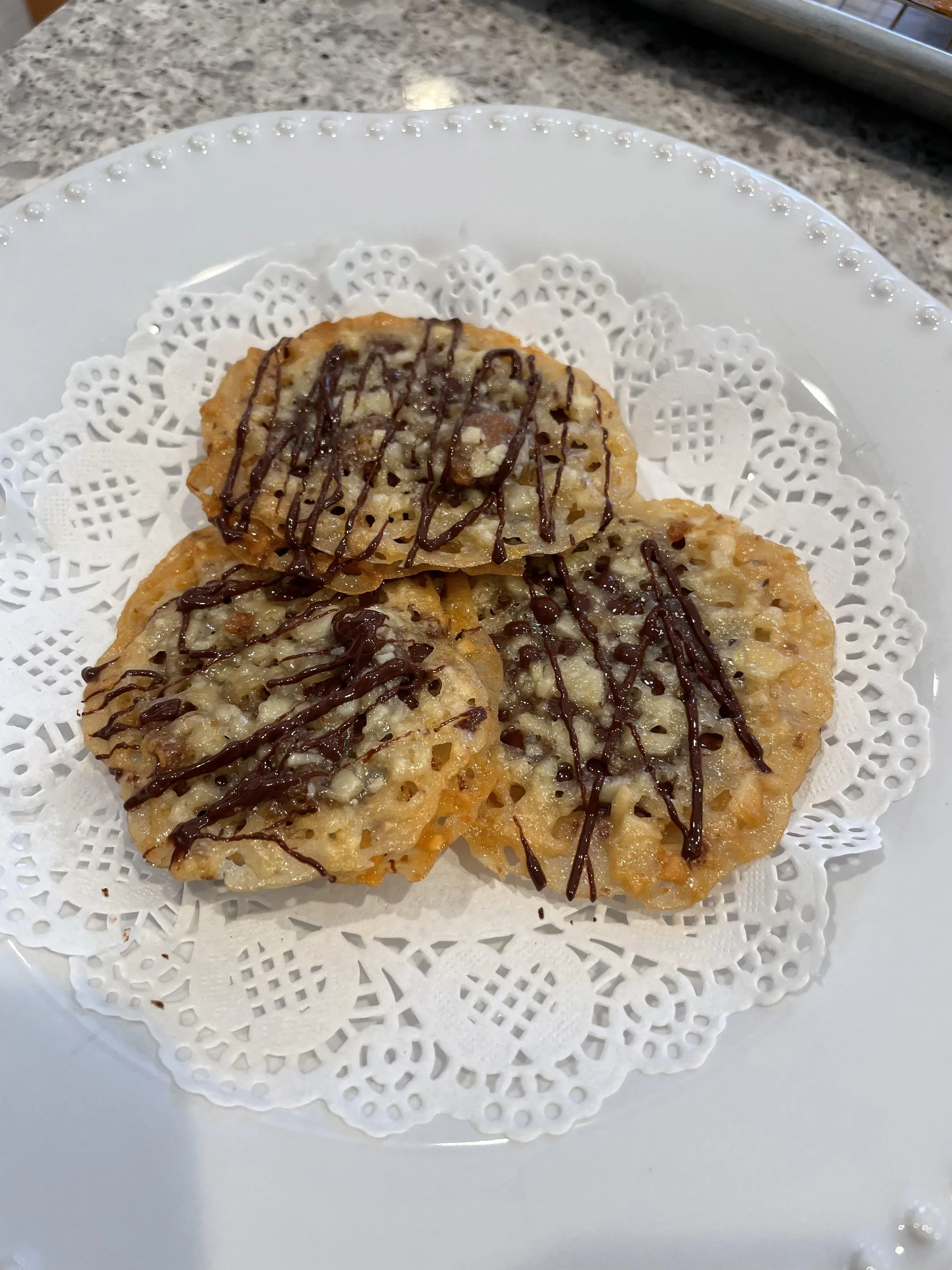 Three fried hash browns topped with chocolate drizzle on a white plate with a paper doily underneath.