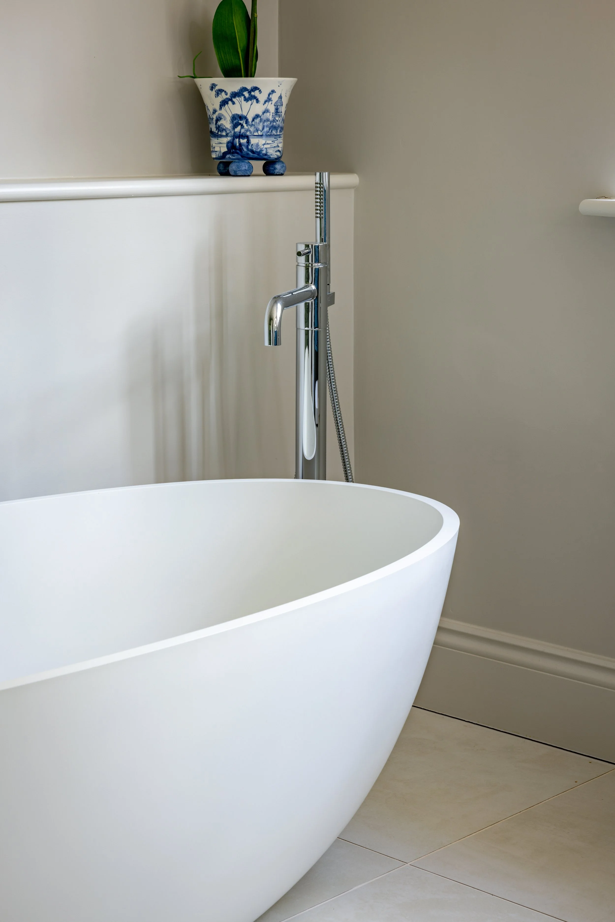 Freestanding white bath with a floor-mounted chrome tap and a blue-and-white vase on the shelf.