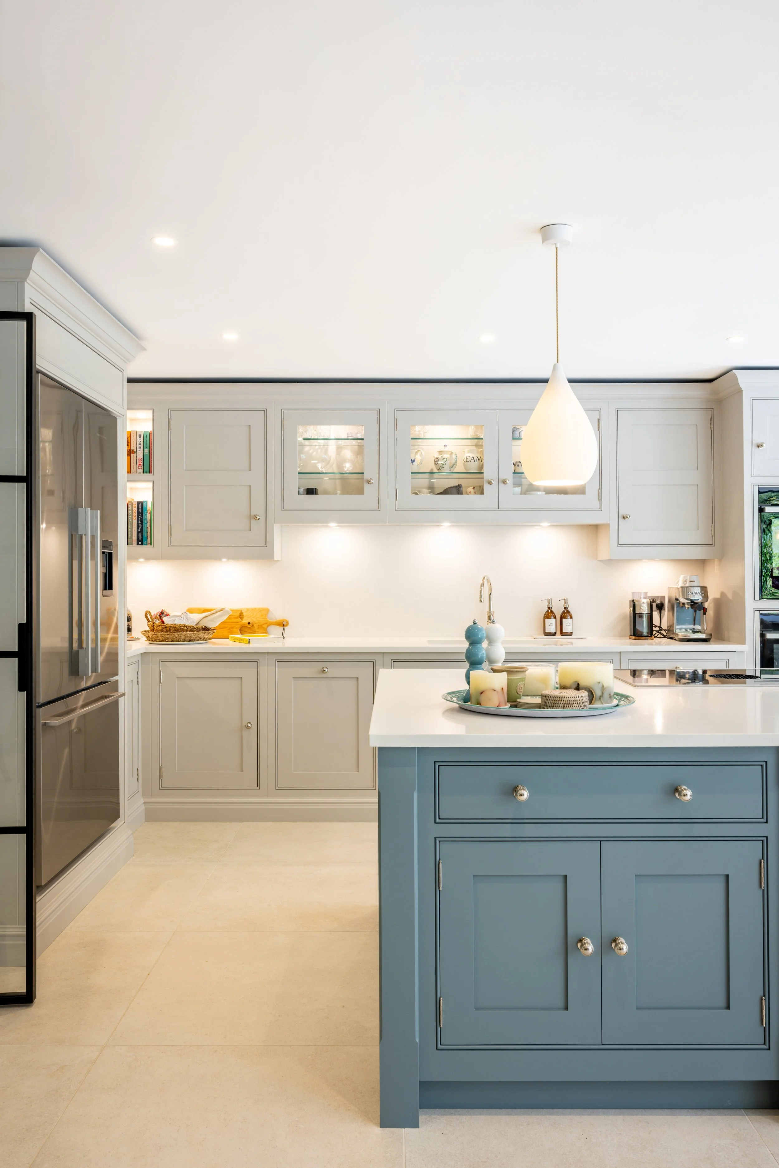View along the blue kitchen island towards pale cabinetry and a pendant light.