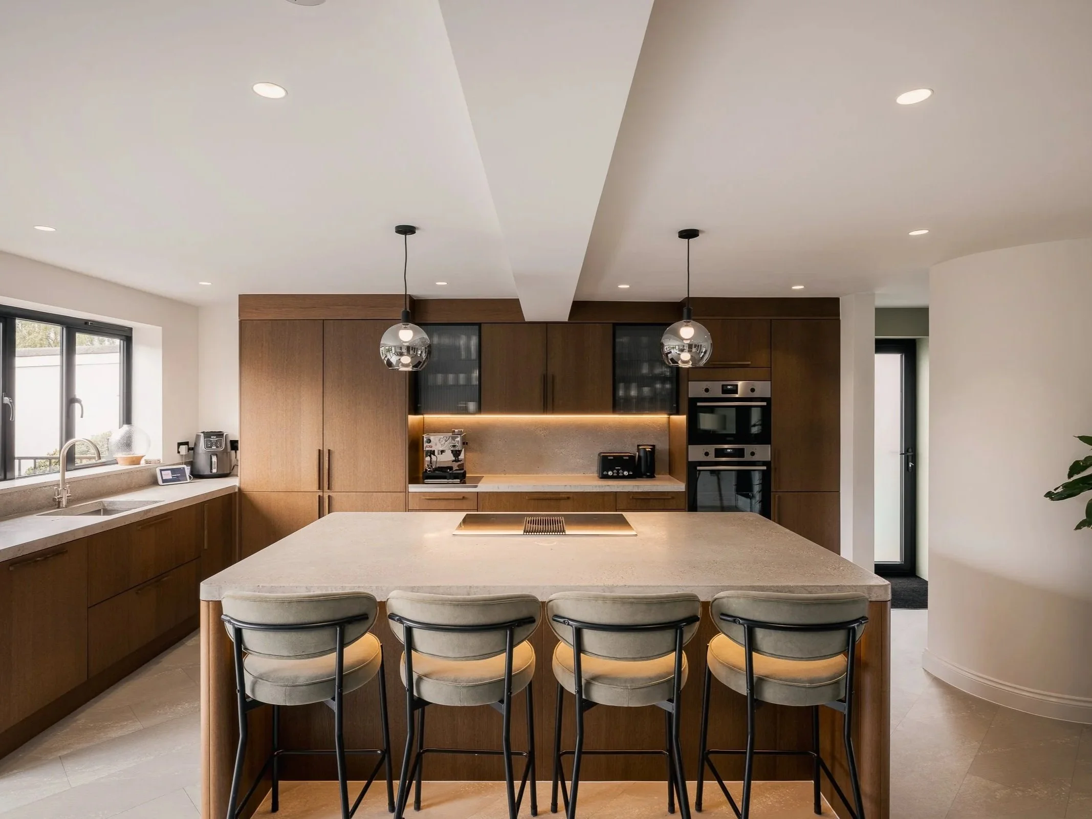 Kitchen with timber cabinetry, a pale island, four bar stools and pendant lights.