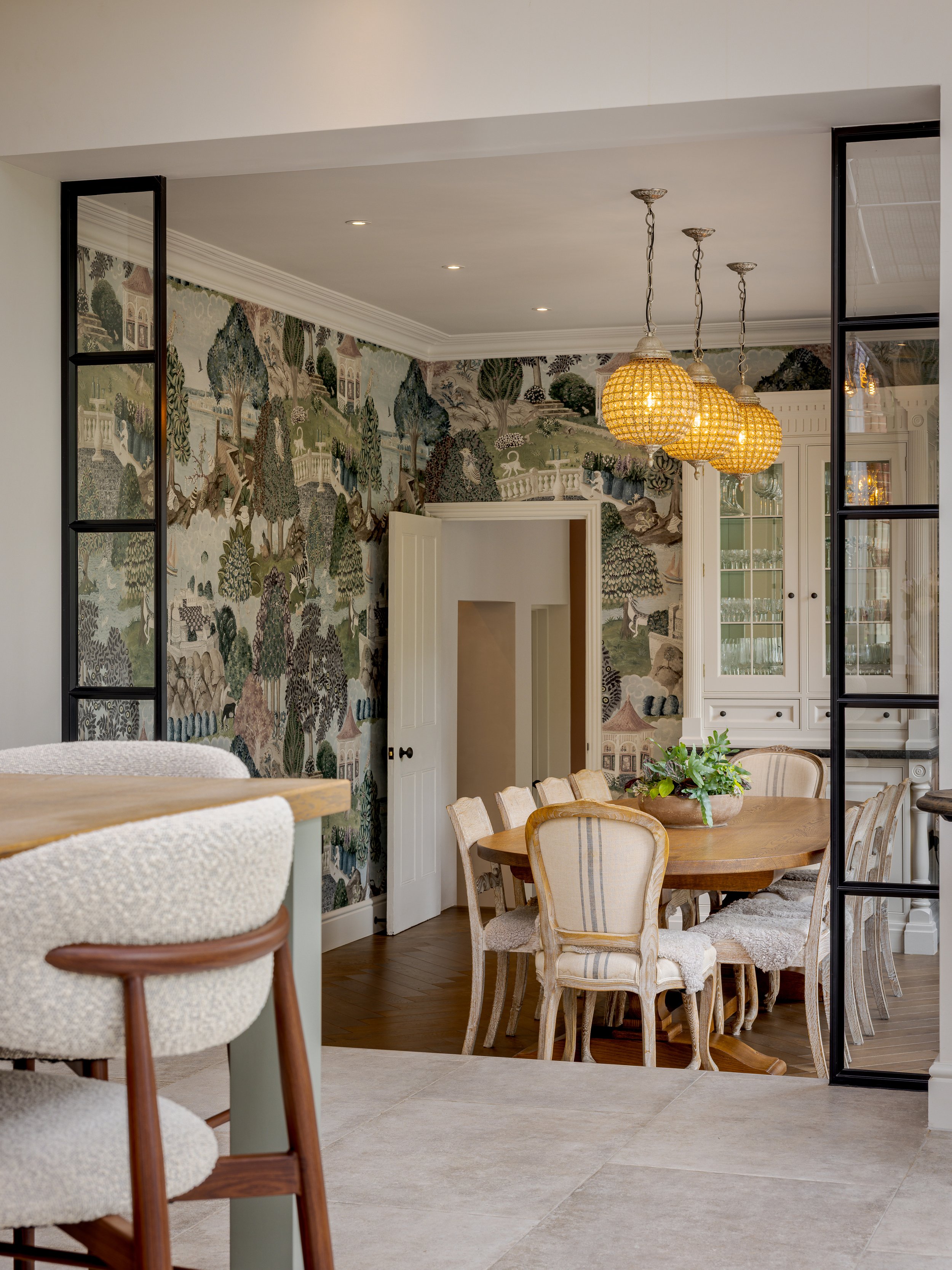 View from the kitchen across a stone worktop and upholstered stool towards the dining room through black-framed glazing at Albury Road