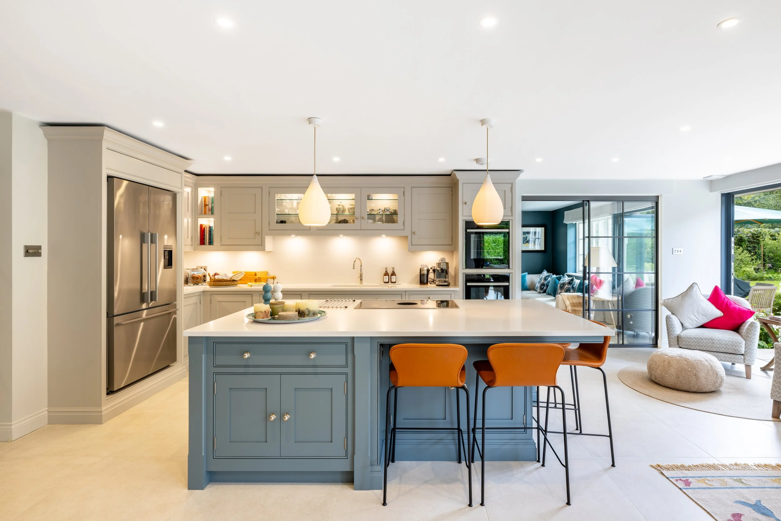 Kitchen island with orange bar stools and three pendant lights, opening towards the garden room.