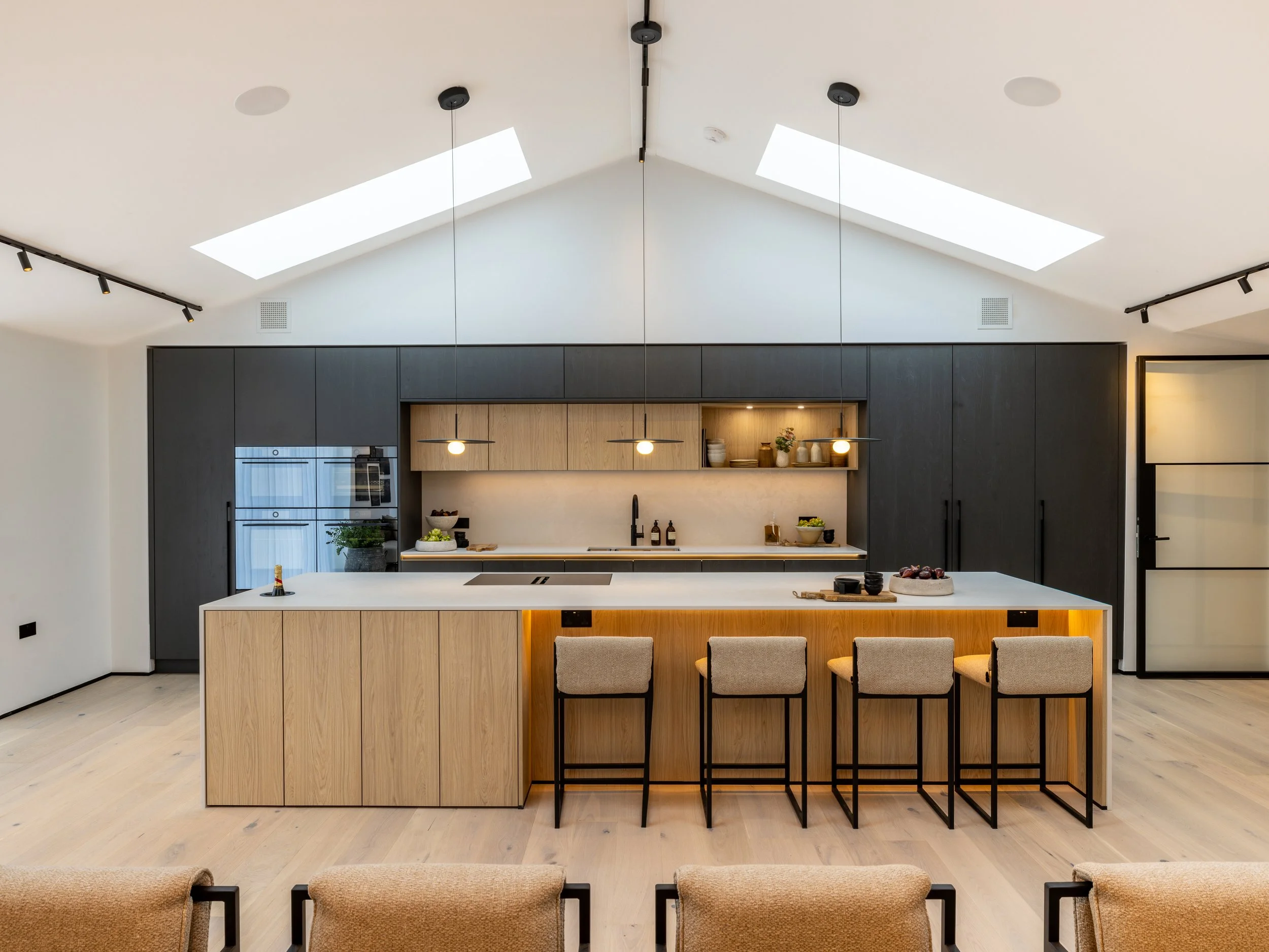Open-plan kitchen and dining space at Hartdene Barns with dark cabinetry, timber beams and pendant lights.