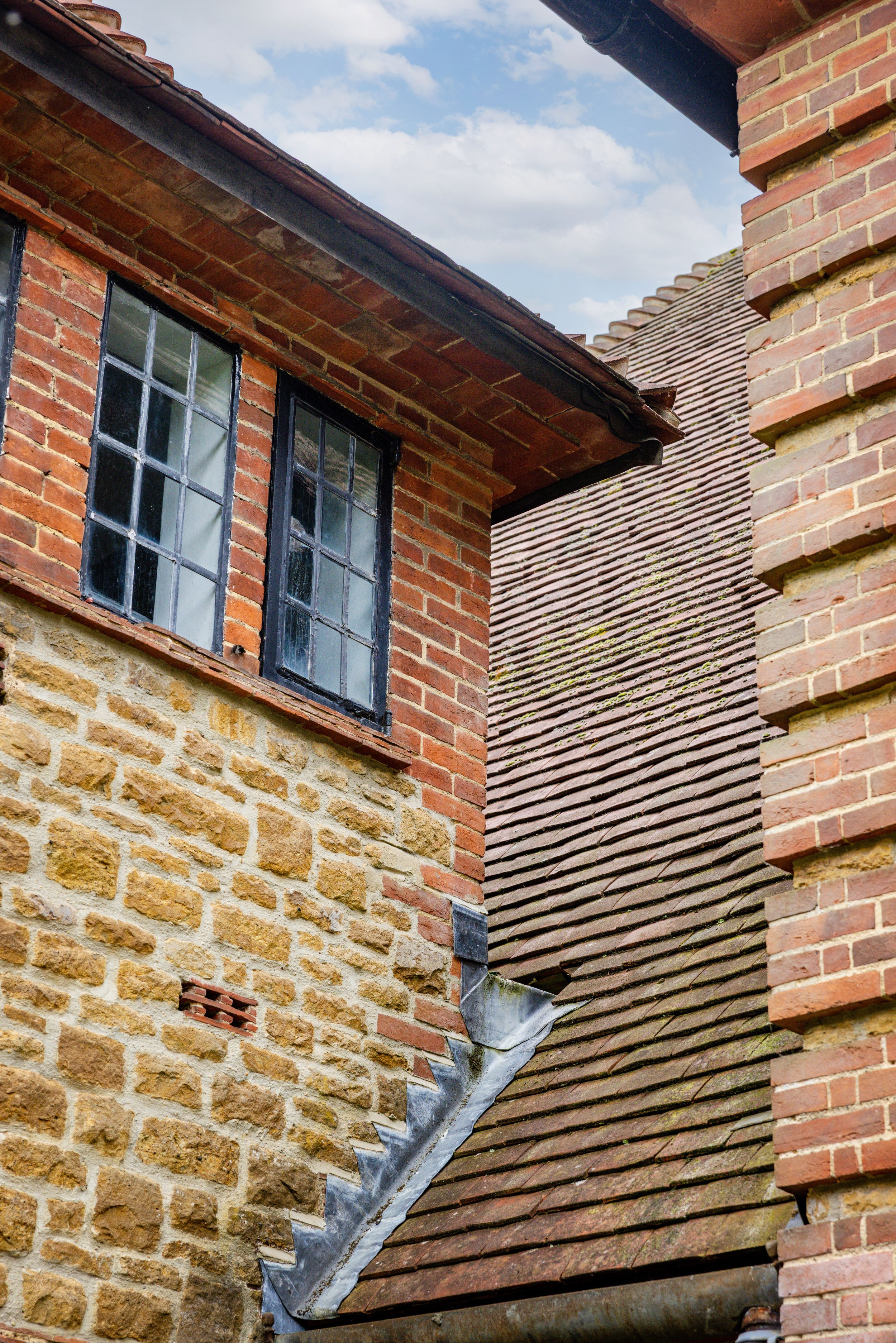 Detail of leaded windows, brick surrounds, stonework and a sweeping tiled roof junction.