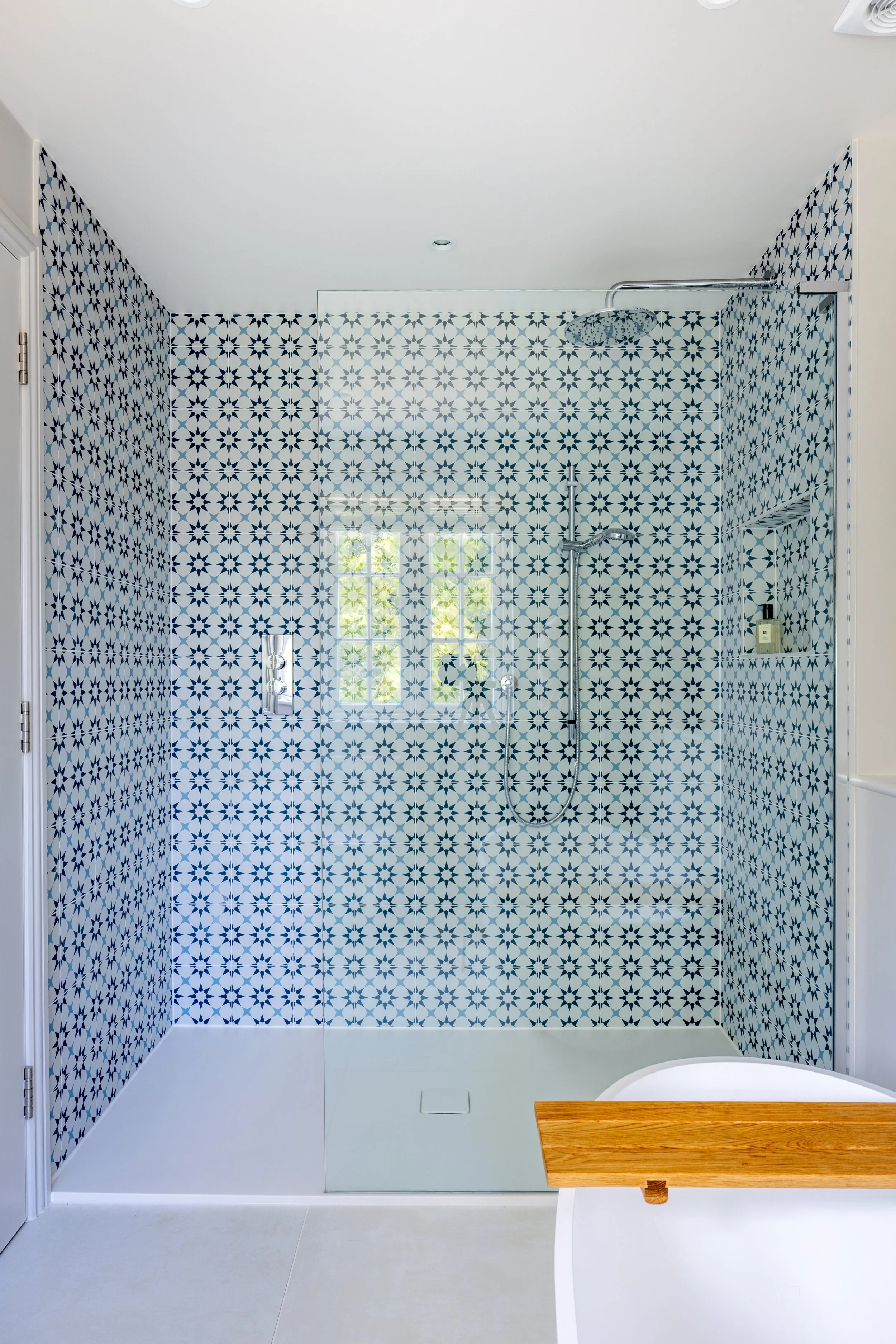 Walk-in shower with small blue-and-white patterned tiles and a glass screen.