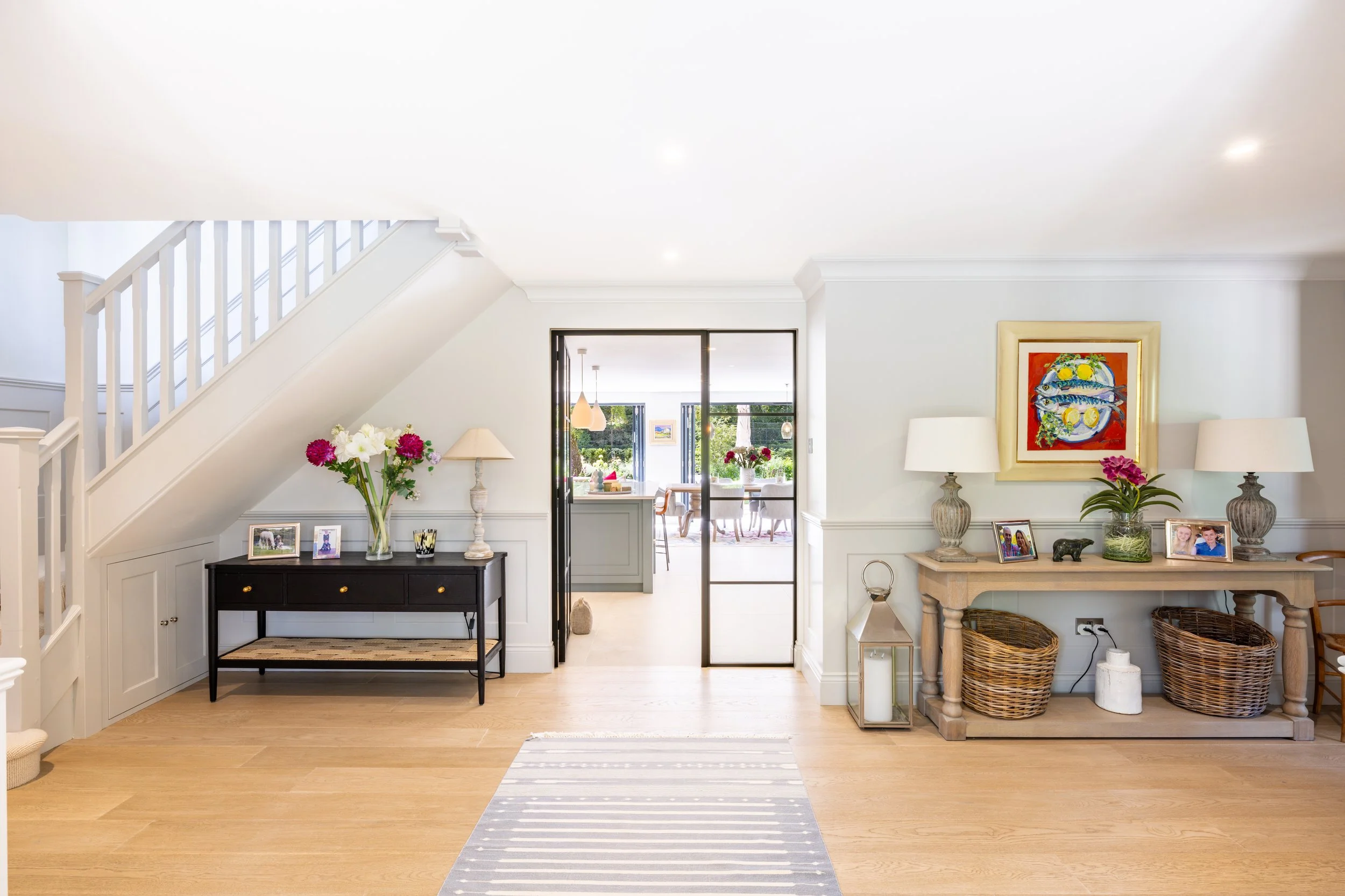 Hallway staircase and console table beside black-framed glazed doors and framed artwork.