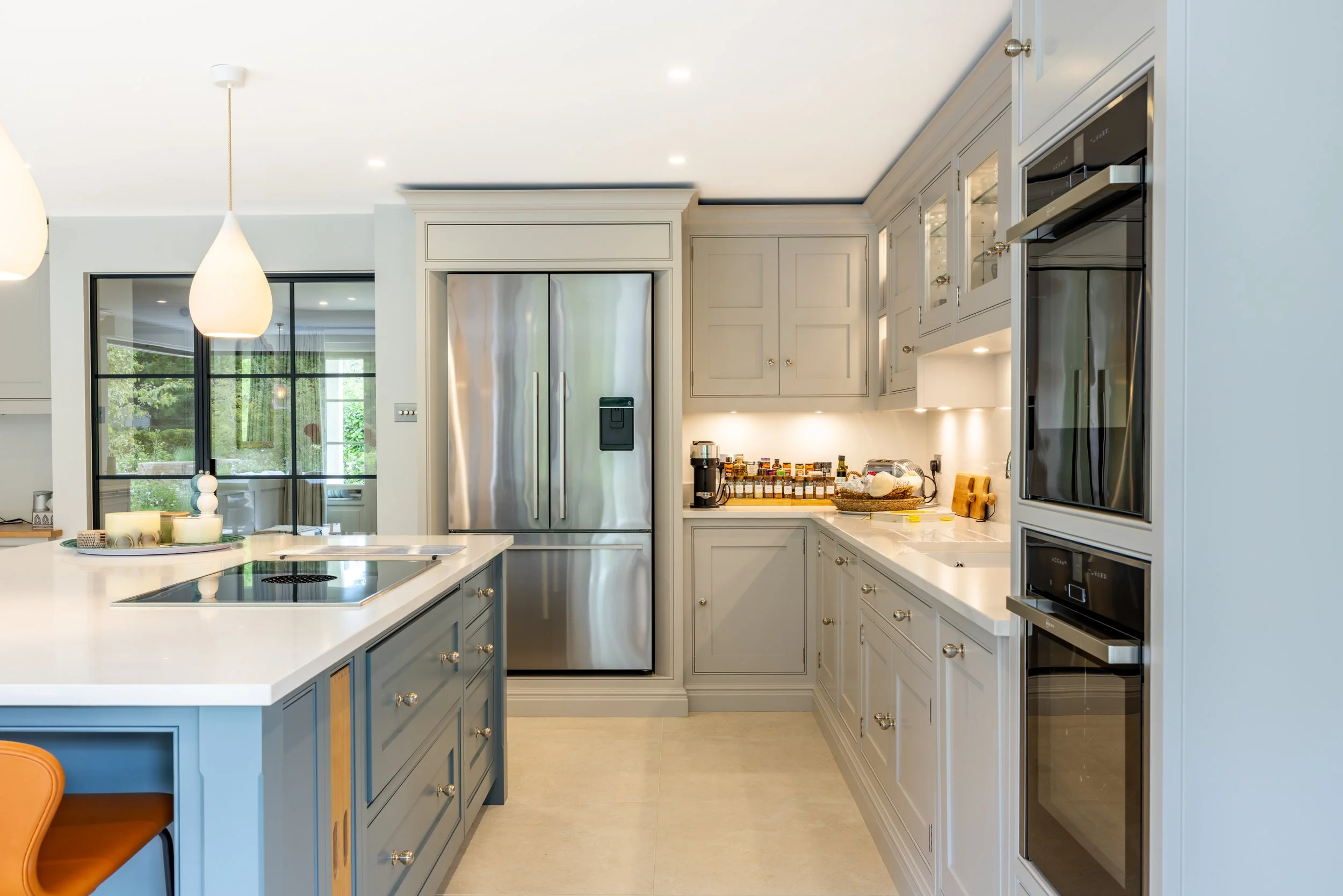 Built-in kitchen cabinetry and ovens beside the island and a black-framed window.
