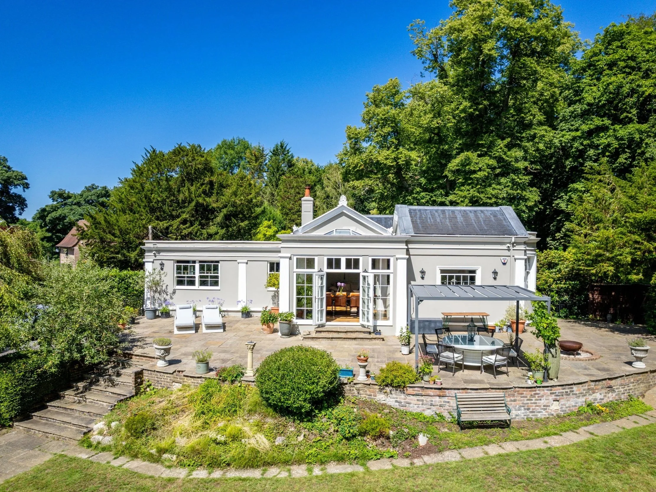 White country home at Tandridge Court Lodge framed by mature trees and a landscaped garden.
