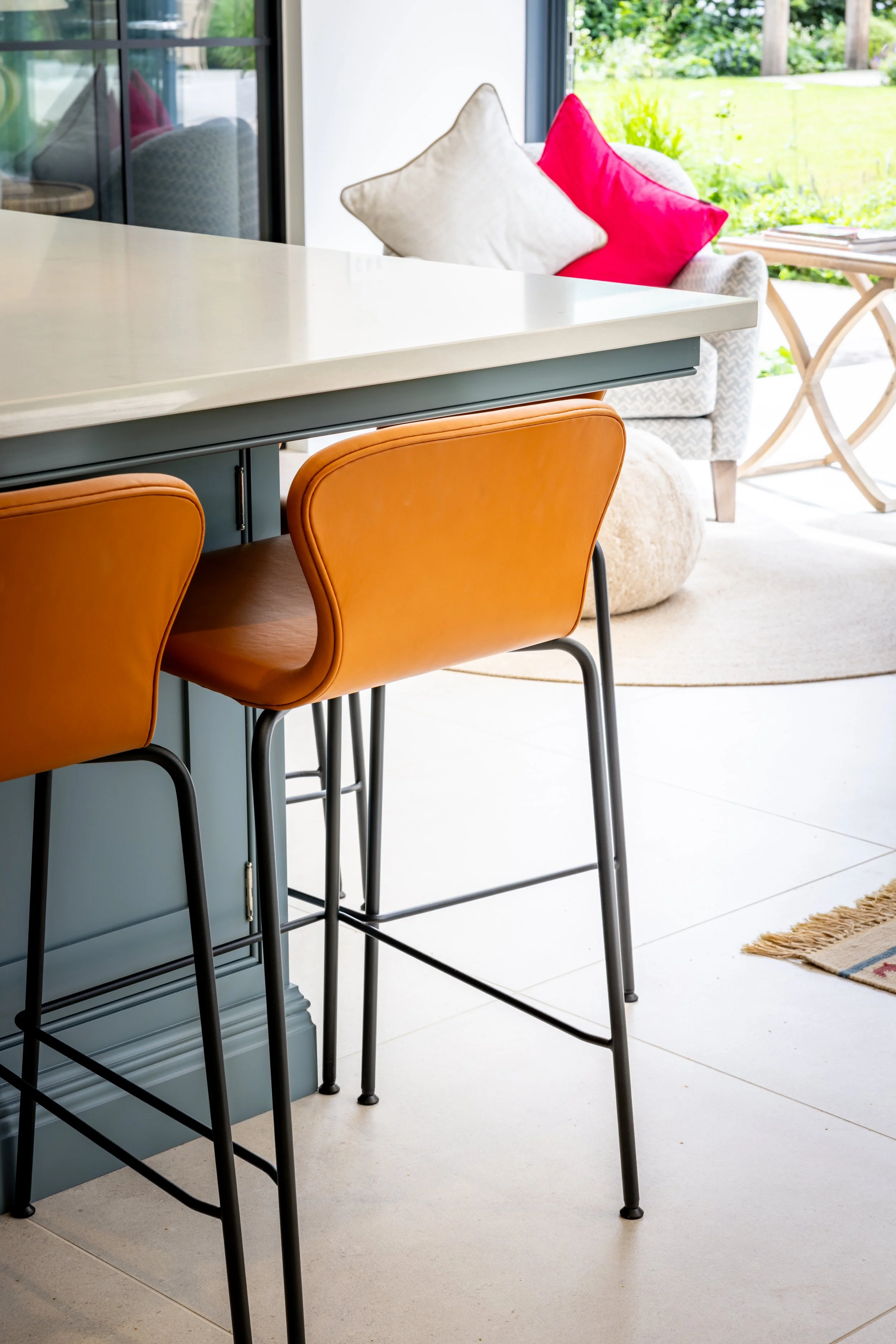 Orange bar stools beneath the island counter, with garden-room seating and glazing beyond.