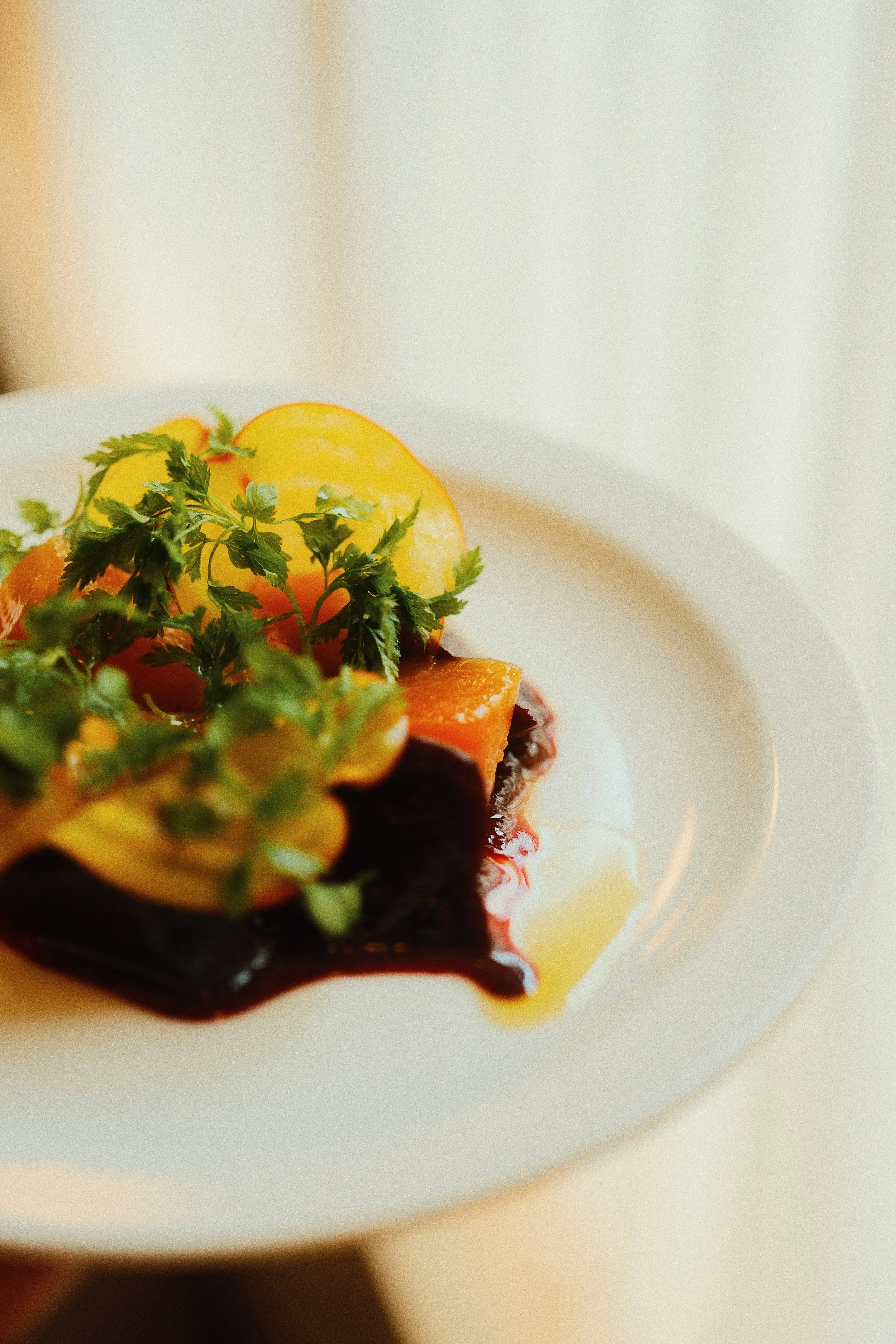 Close-up of a plate with roasted sweet potatoes, garnished with fresh herbs, and drizzled with sauce.