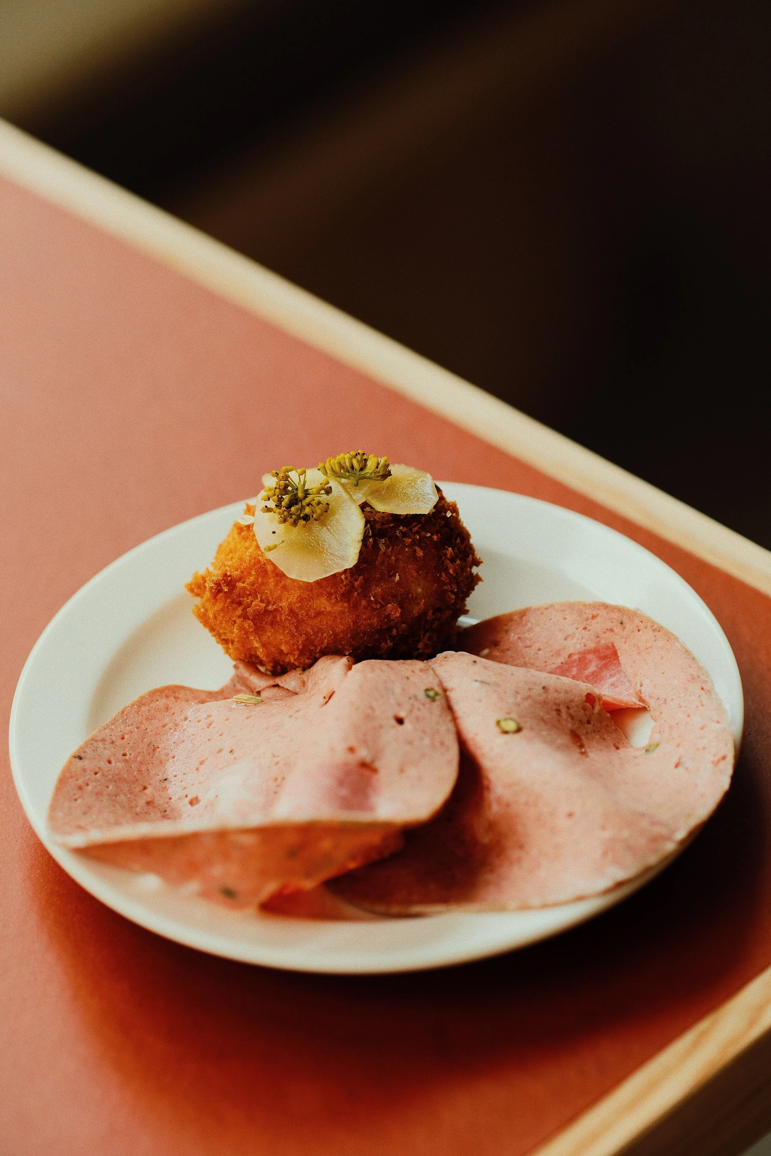 Sliced deli ham on a white plate, garnished with herbs, on a pinkish surface.