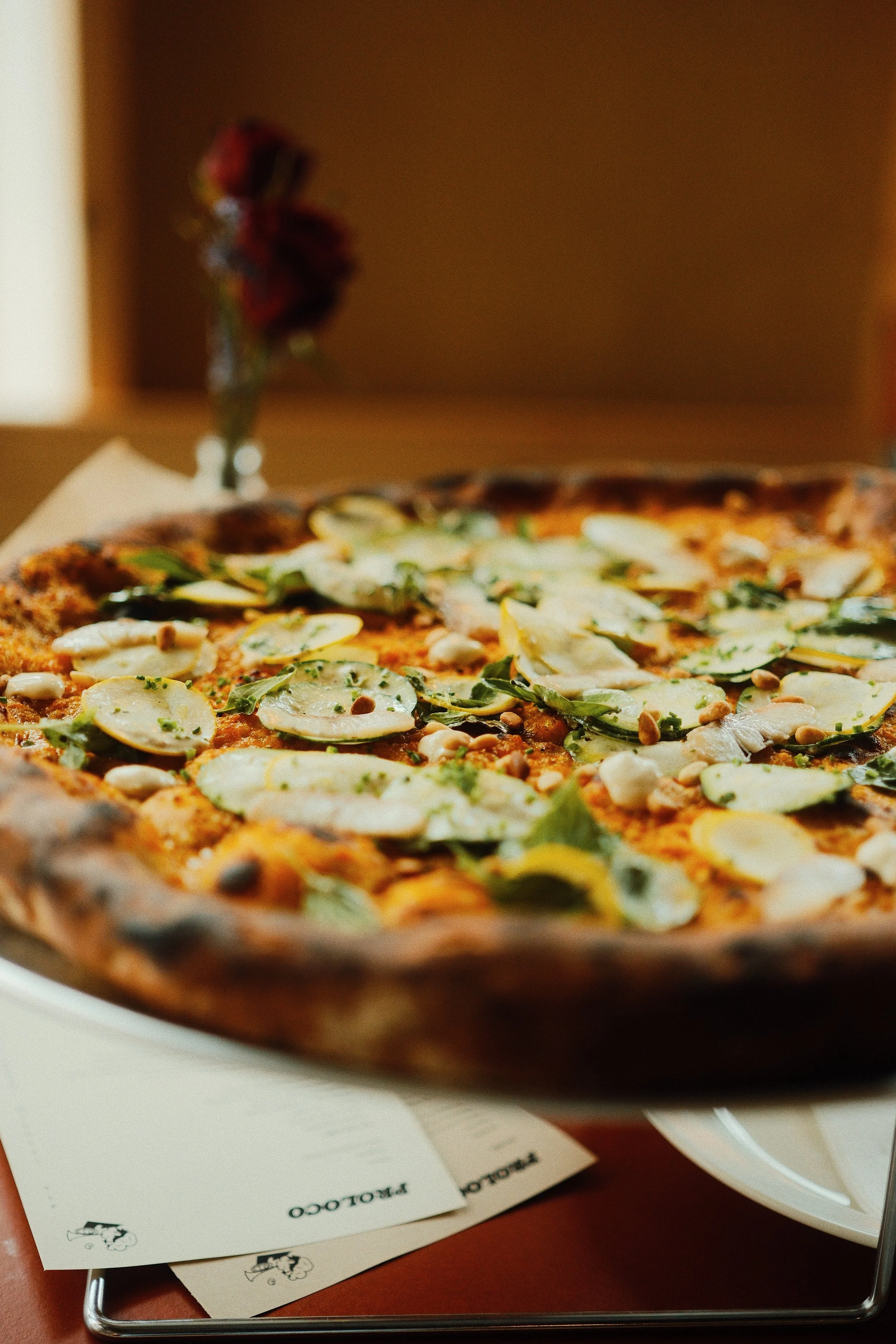 Close-up of a pizza with sliced cheese, herbs, and other toppings on a tray. A menu is partially visible underneath the tray.