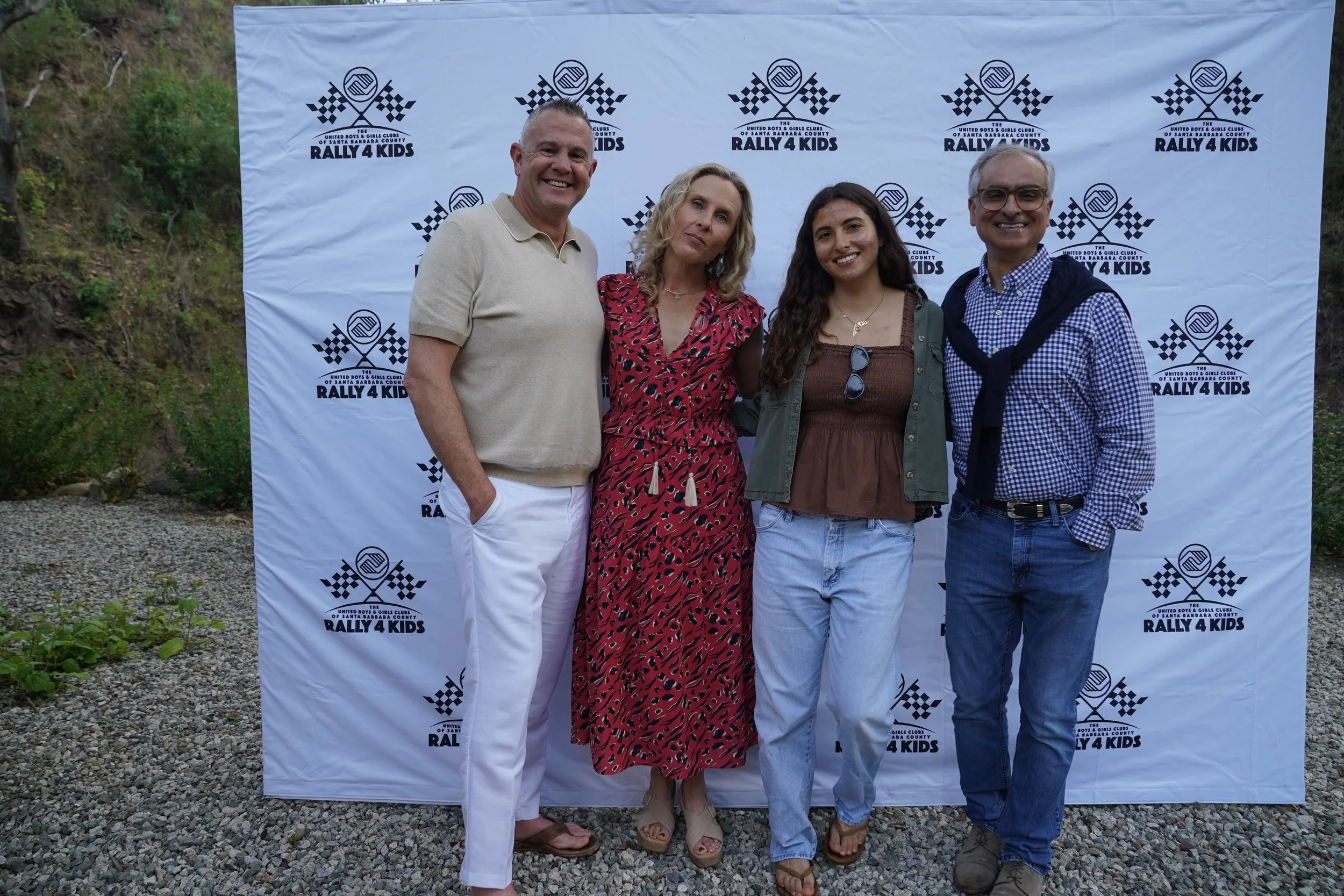Four people standing outdoors in front of a Rally 4 Kids backdrop, smiling for the camera.