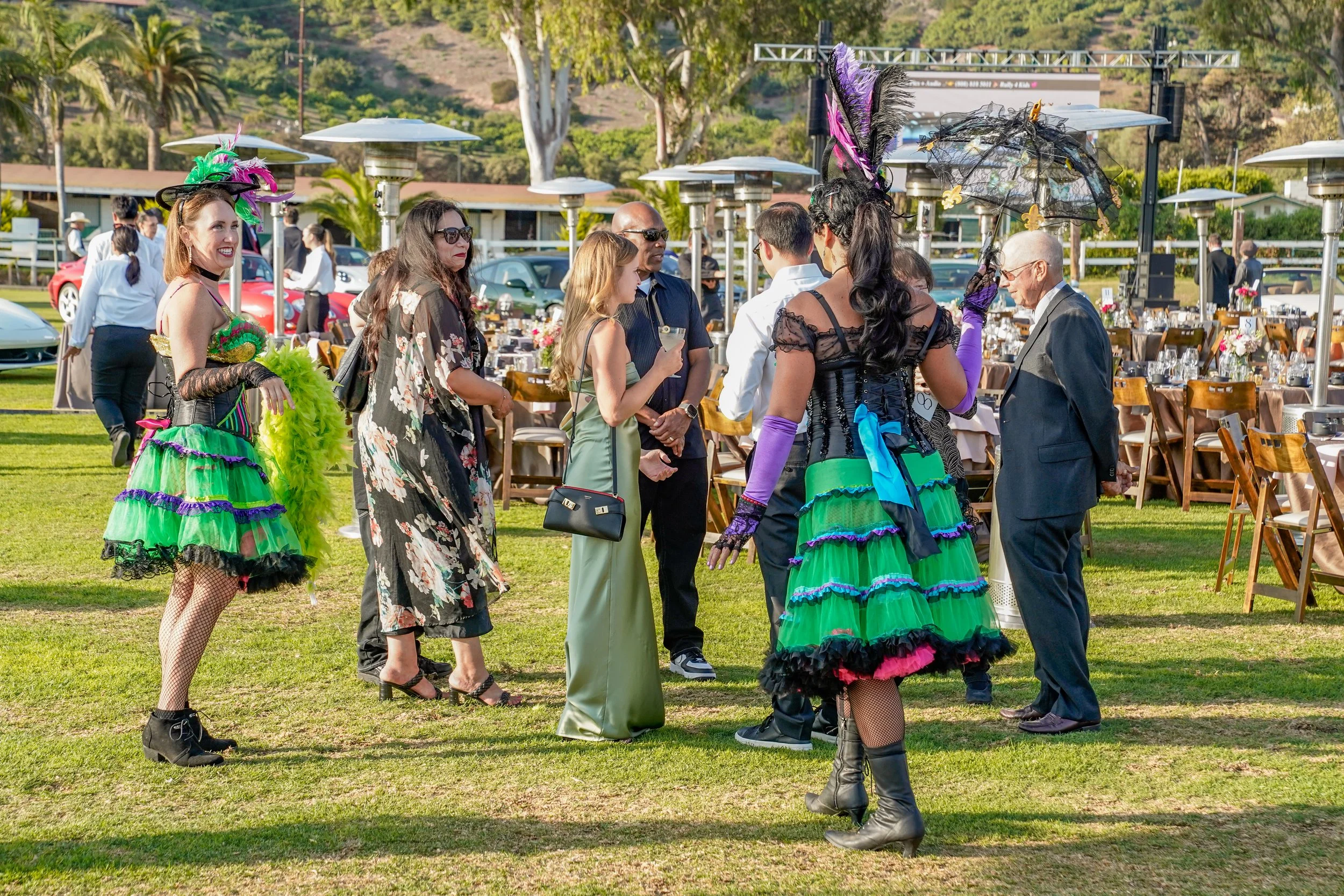 People socializing outdoors at a formal event with tables, chairs, and ambient lighting, dressed in colorful and elegant attire.