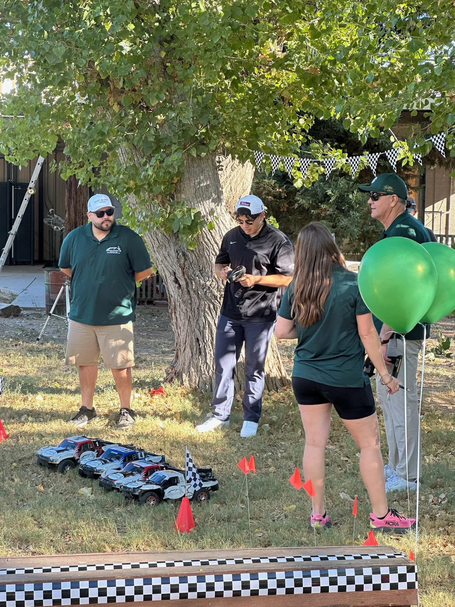 four-people-standing-near-rc-cars-under-a-tree-with-green-balloons--0da5cb9e.jpeg