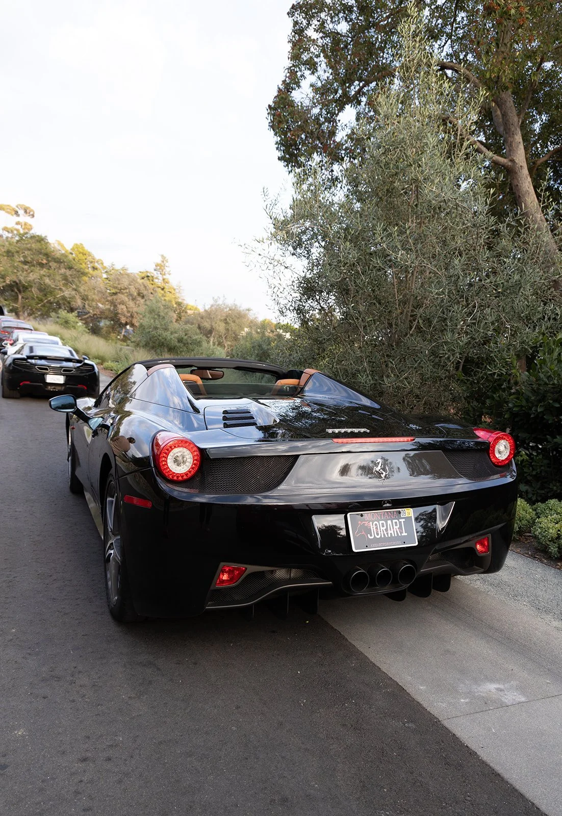 A black Ferrari convertible parked on a street with green trees in the background.