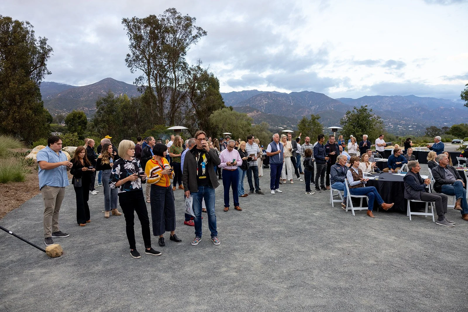 Group of people attending an outdoor event with mountainous landscape in the background.