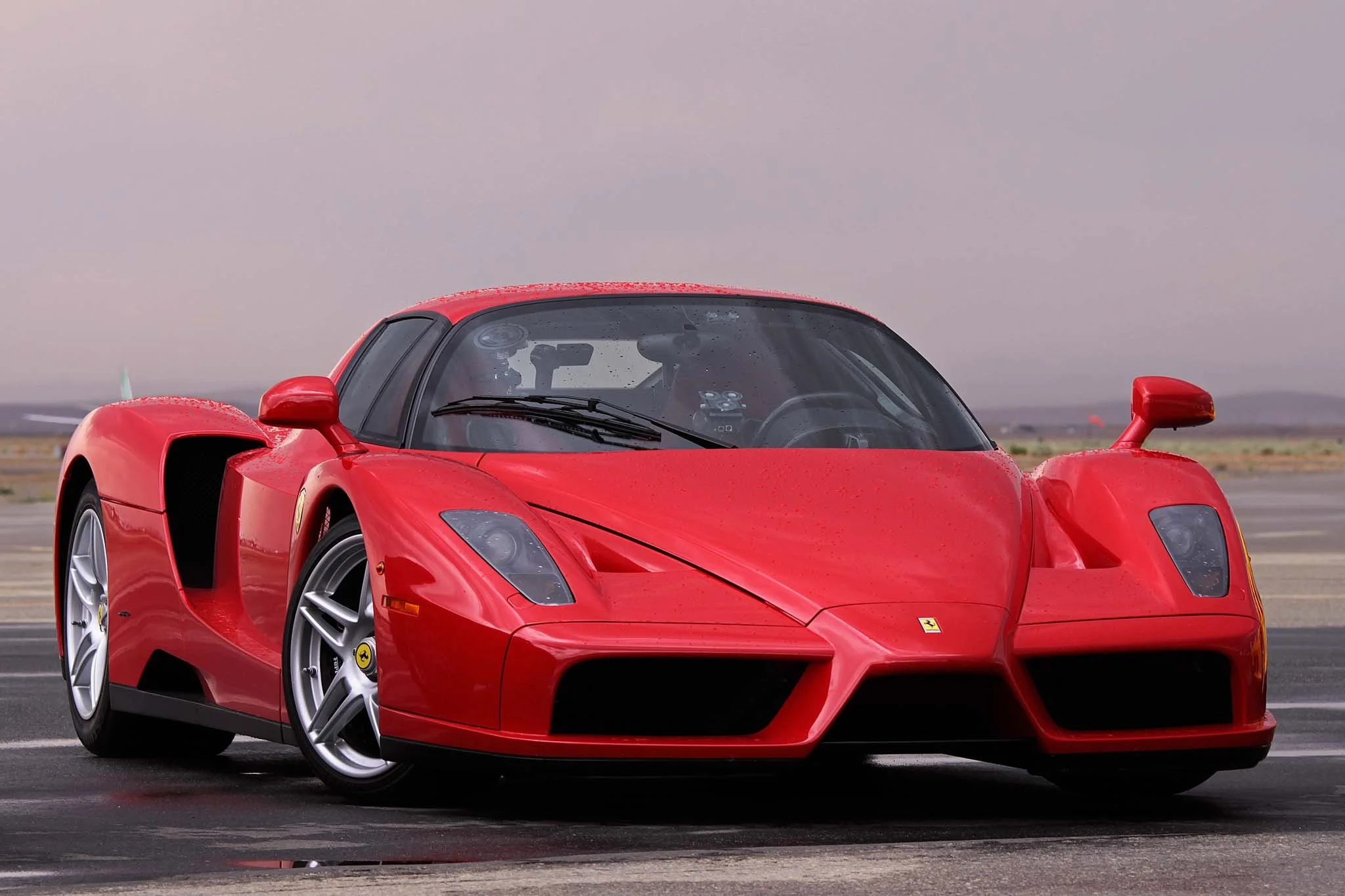 Red Ferrari sports car on a racetrack with a cloudy sky in the background.
