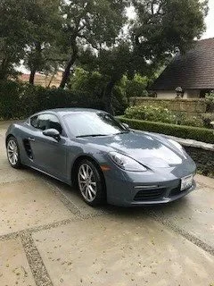 Gray sports car parked on a driveway with trees and a house in the background.
