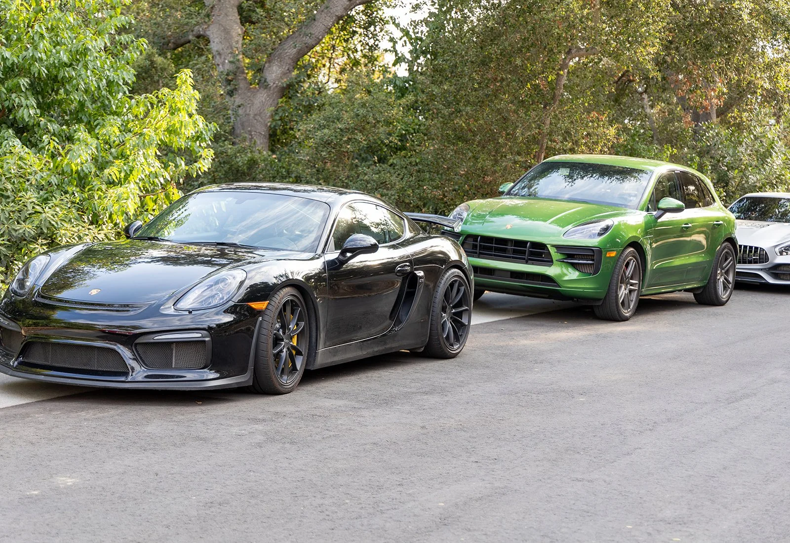 A black sports car and a green SUV parked on the side of the road with trees and bushes in the background.