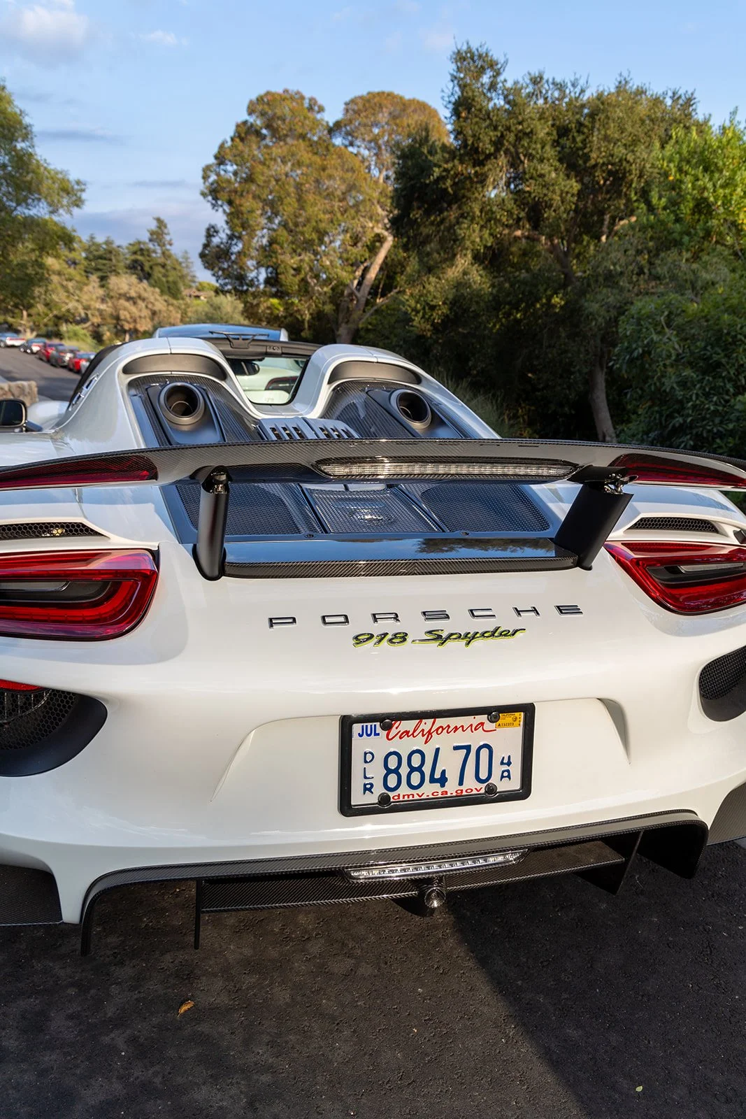 Rear view of a white Porsche 918 Spyder sports car with a large rear wing, exposed engine components, and California license plate.