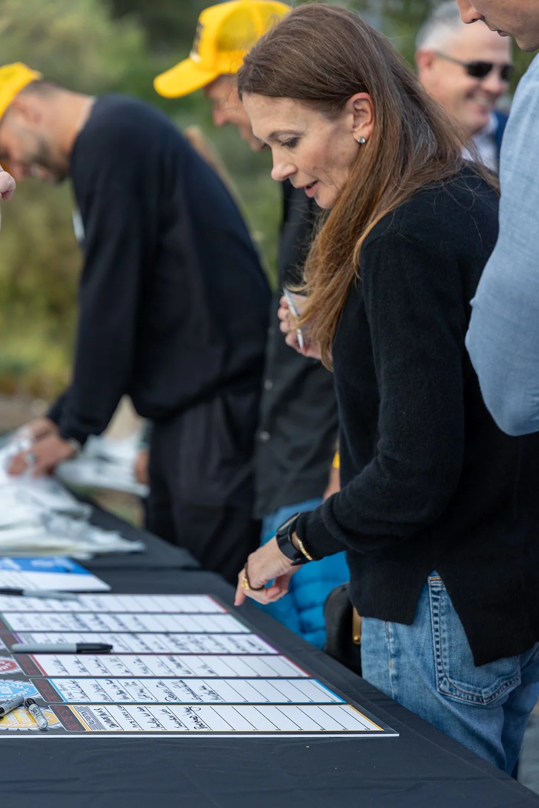 People gathered around a table outdoors, signing or reviewing papers on a black tablecloth.