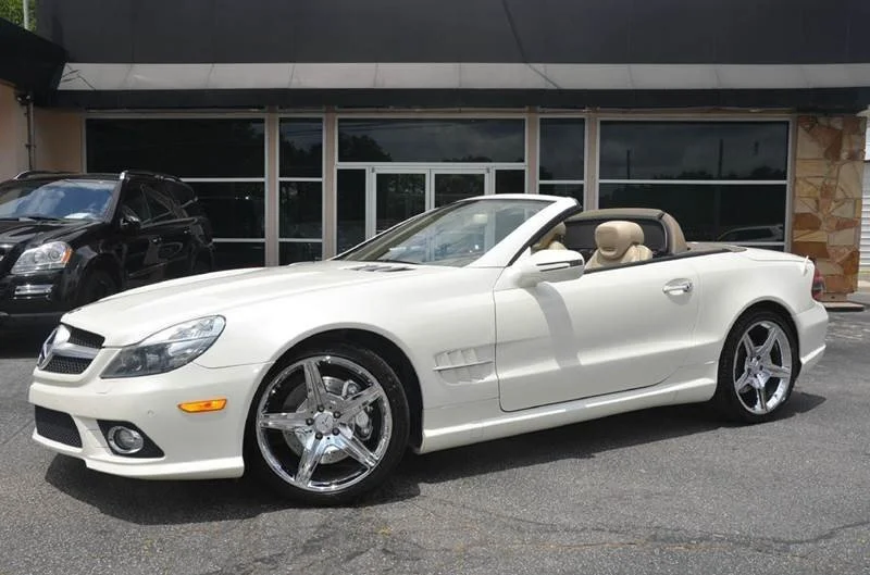 White convertible sports car with beige interior and large chrome wheels parked in front of a commercial building.