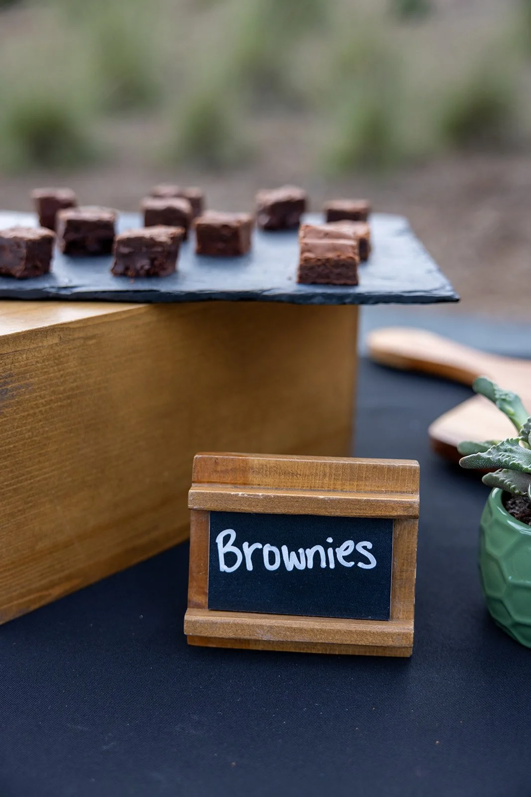 Chocolate brownies on a slate platter with a blackboard sign that says 'Brownies' in front of a wooden stand.
