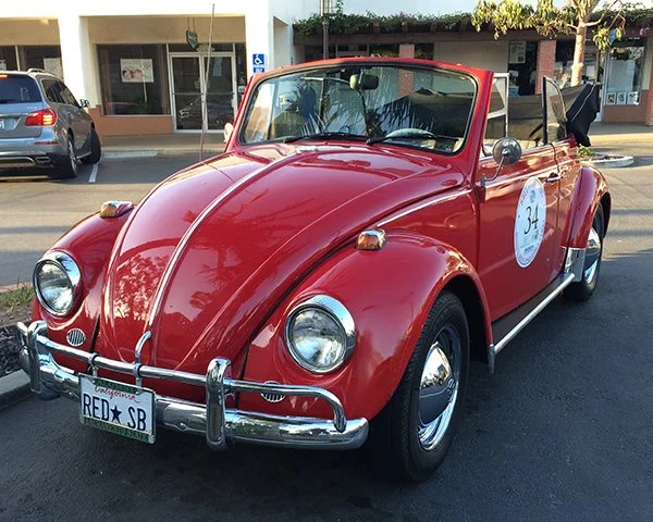 Red vintage Volkswagen Beetle convertible parked on a street.