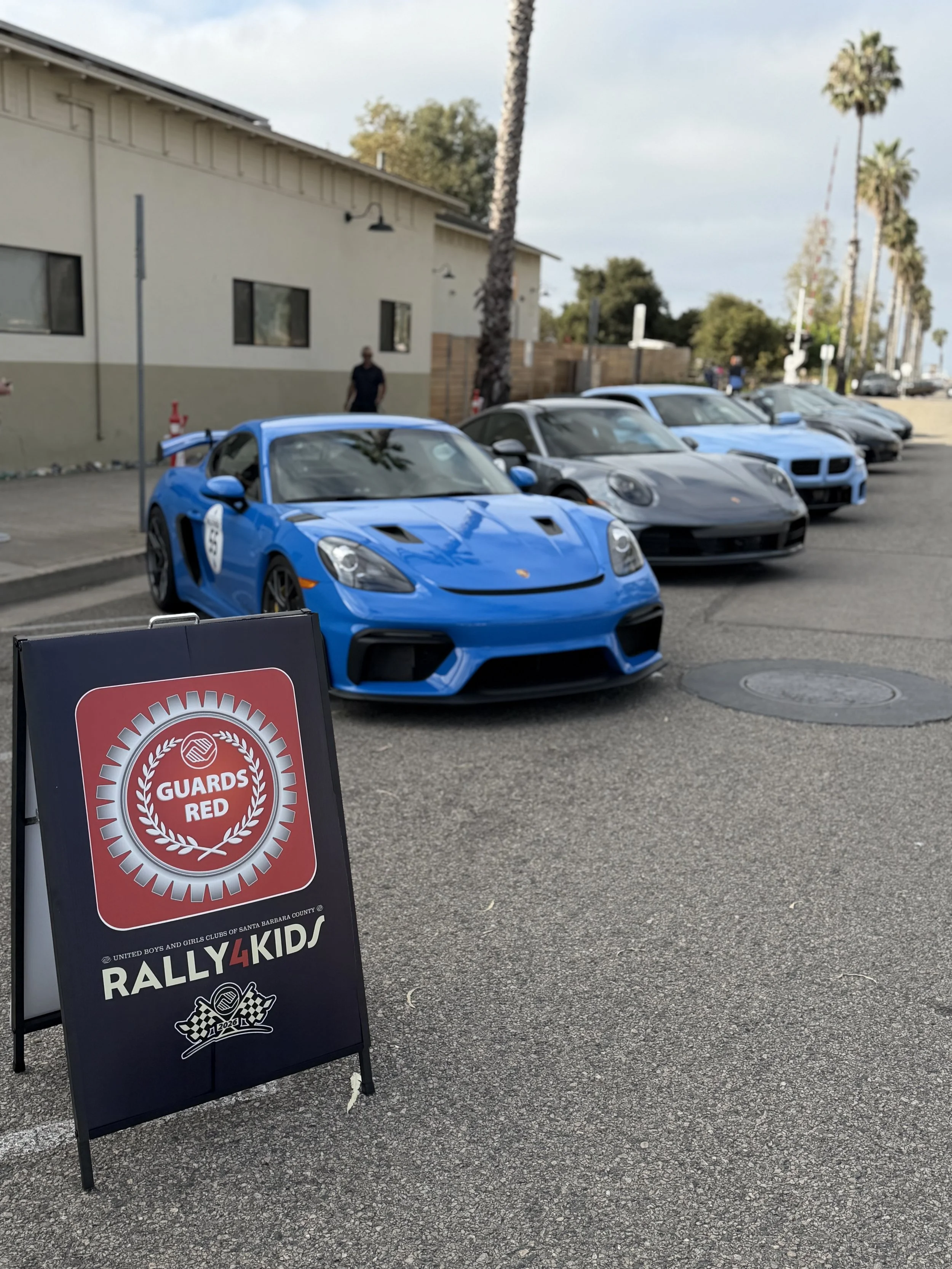 blue-porsche-beside-rally4kids-sign-and-parked-convertibles--558539ea.jpeg
