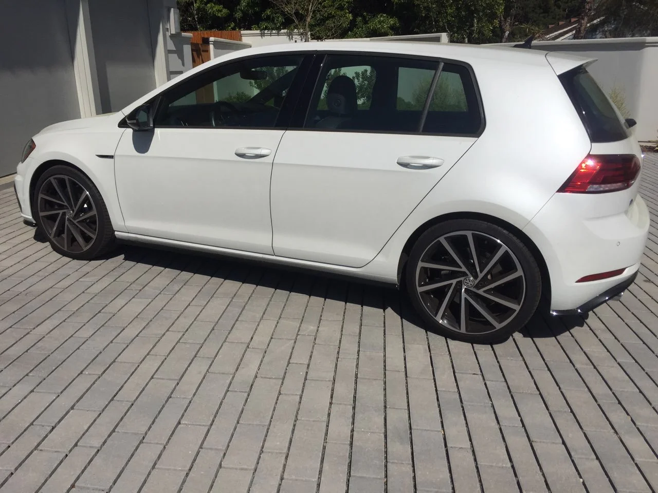 White modern hatchback Volkswagen car parked on a paved driveway with garage and greenery in the background.