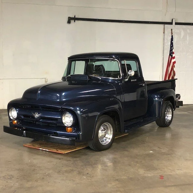 Vintage navy blue pickup truck with an American flag in the background inside a warehouse.