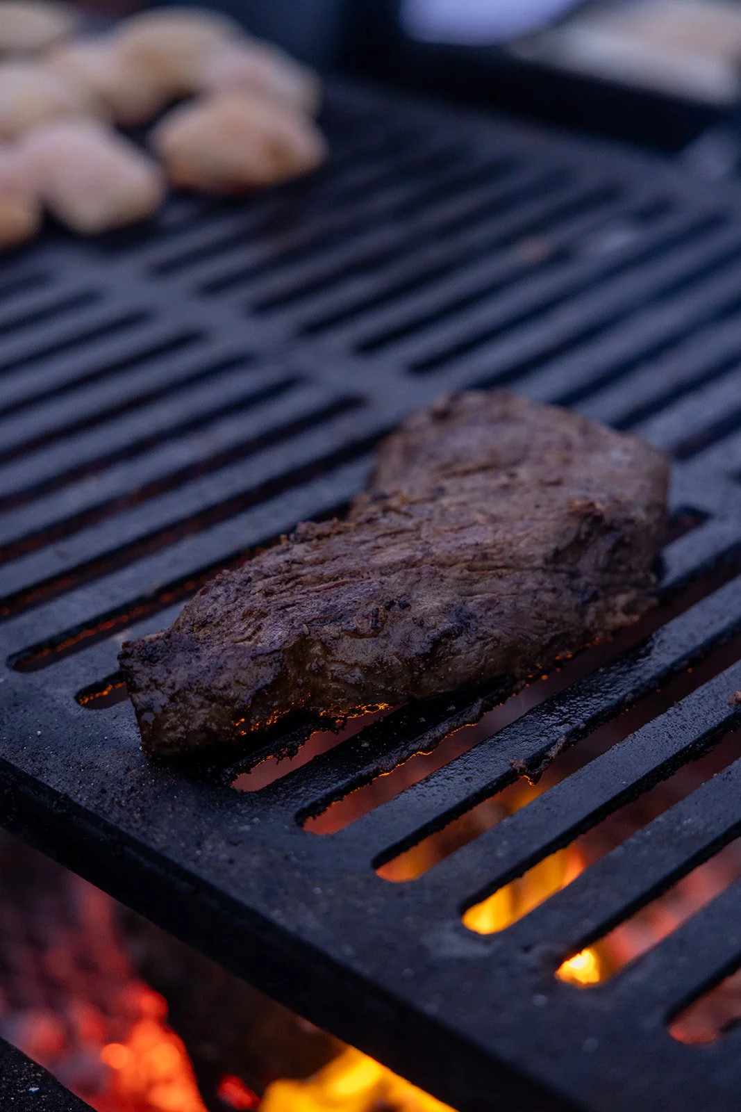 A piece of steak being grilled on a barbecue with flames visible underneath.