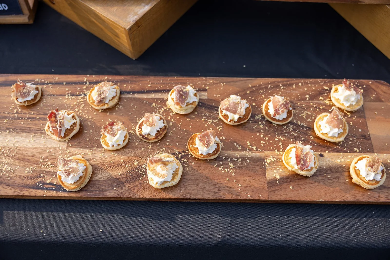 Small appetizers with cream cheese and prosciutto on a wooden serving board.