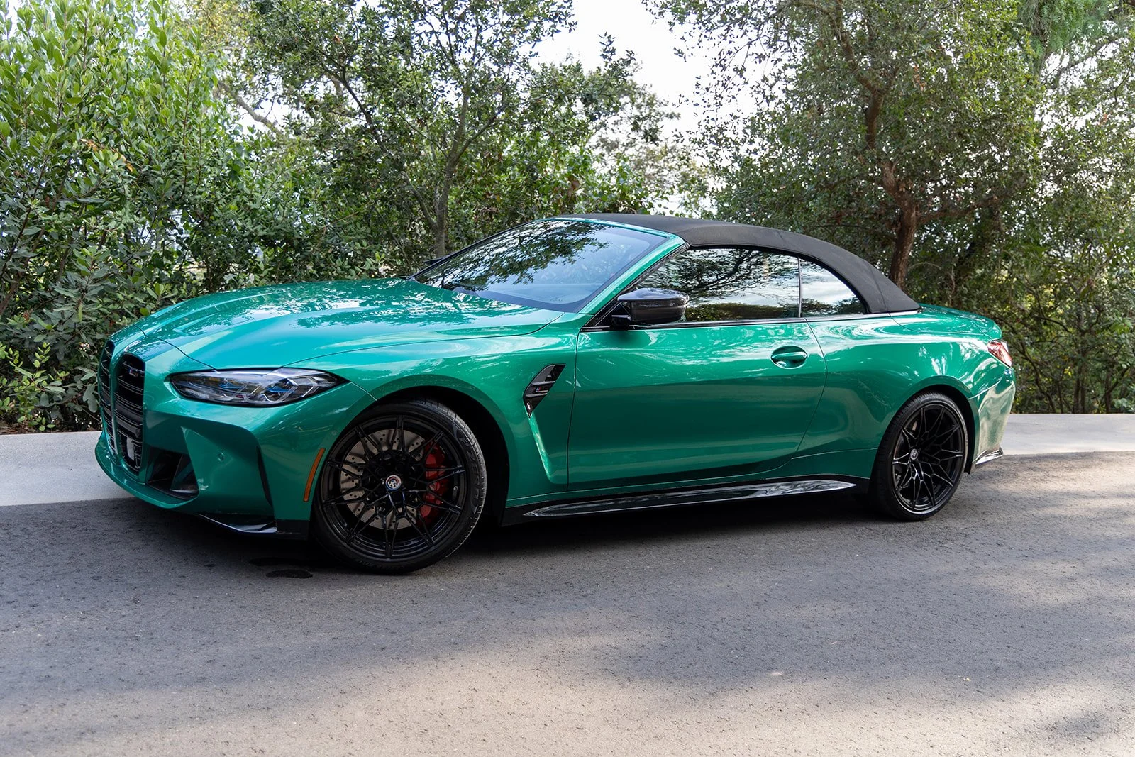 A green convertible sports car parked on the side of a road with trees and foliage in the background.