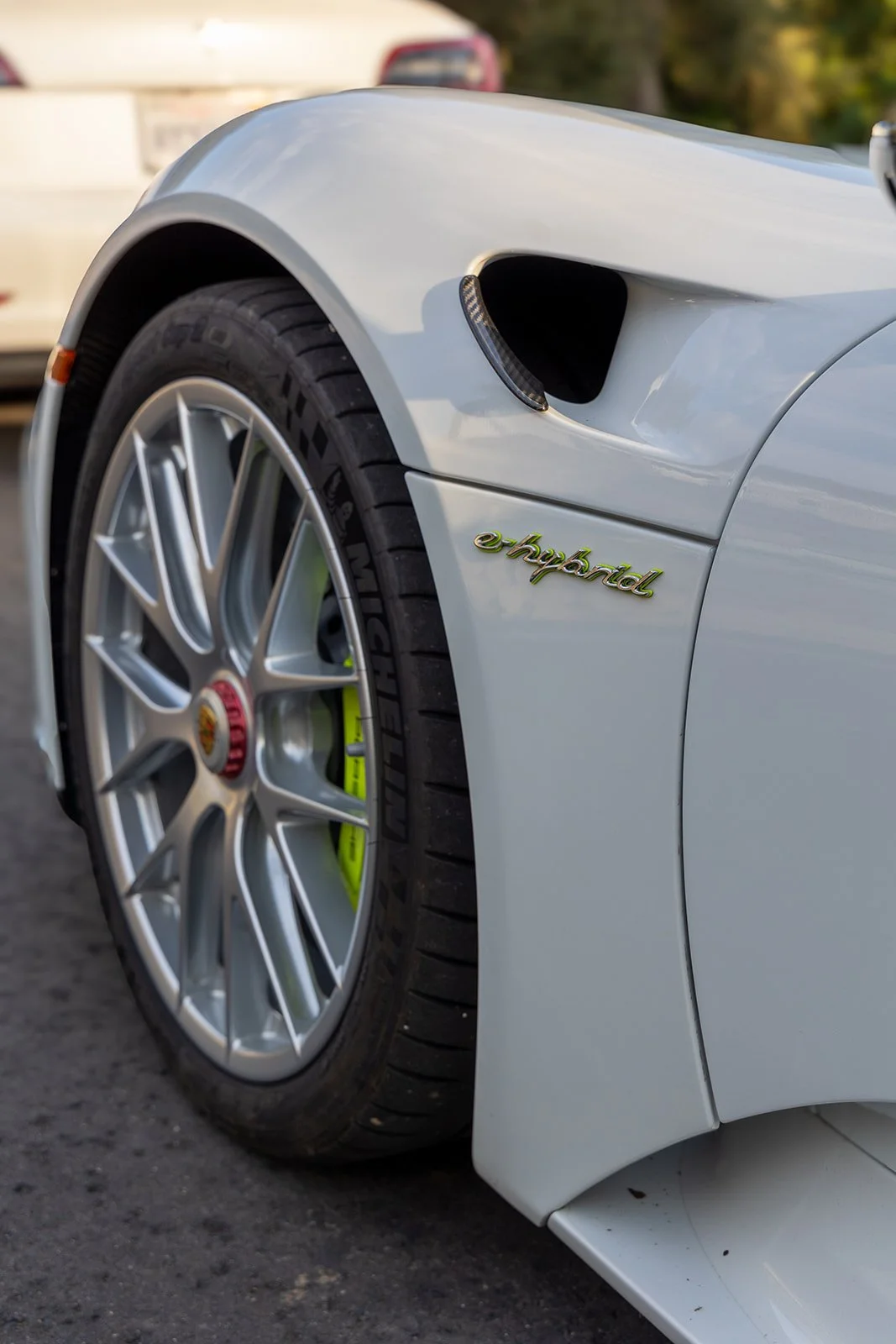 Close-up of a white luxury sports car with a Porsche crest on the wheel, featuring a yellow brake caliper and the model badge 'e-hybrid' on the side.