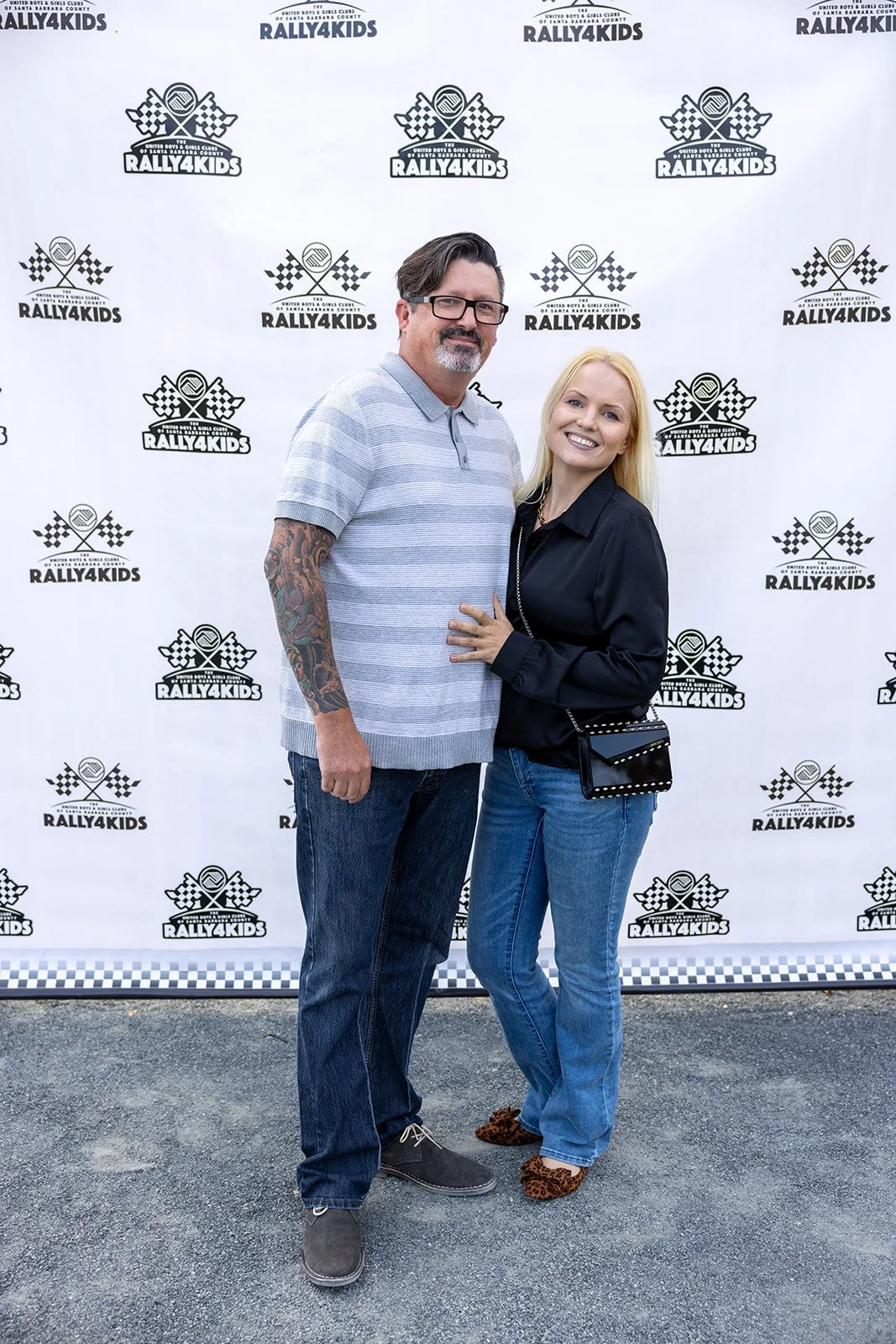 A man and woman posing together in front of a Rally4Kids backdrop at an event, smiling for the camera.