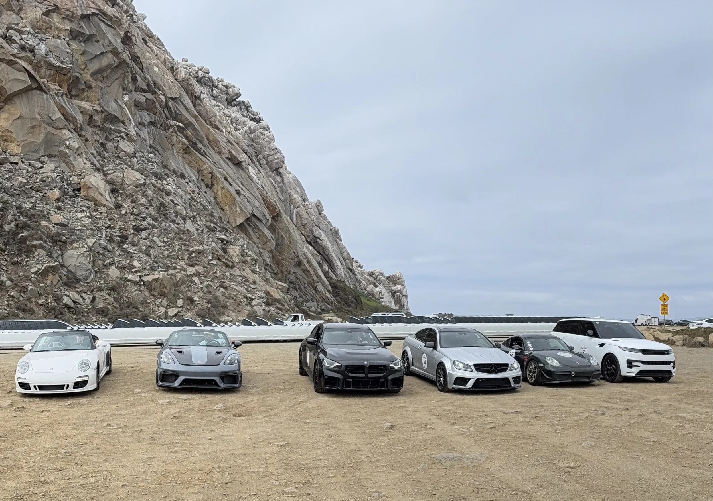 six-luxury-cars-parked-on-dirt-near-rocky-cliff--b904282b.jpeg