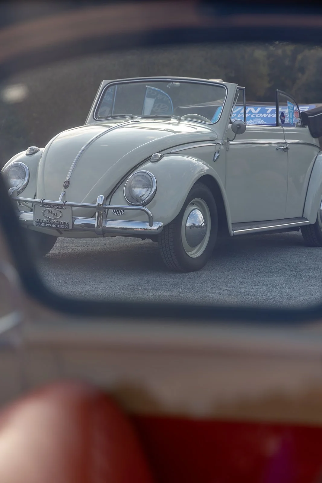 Vintage white Volkswagen Beetle convertible viewed through a car side mirror.