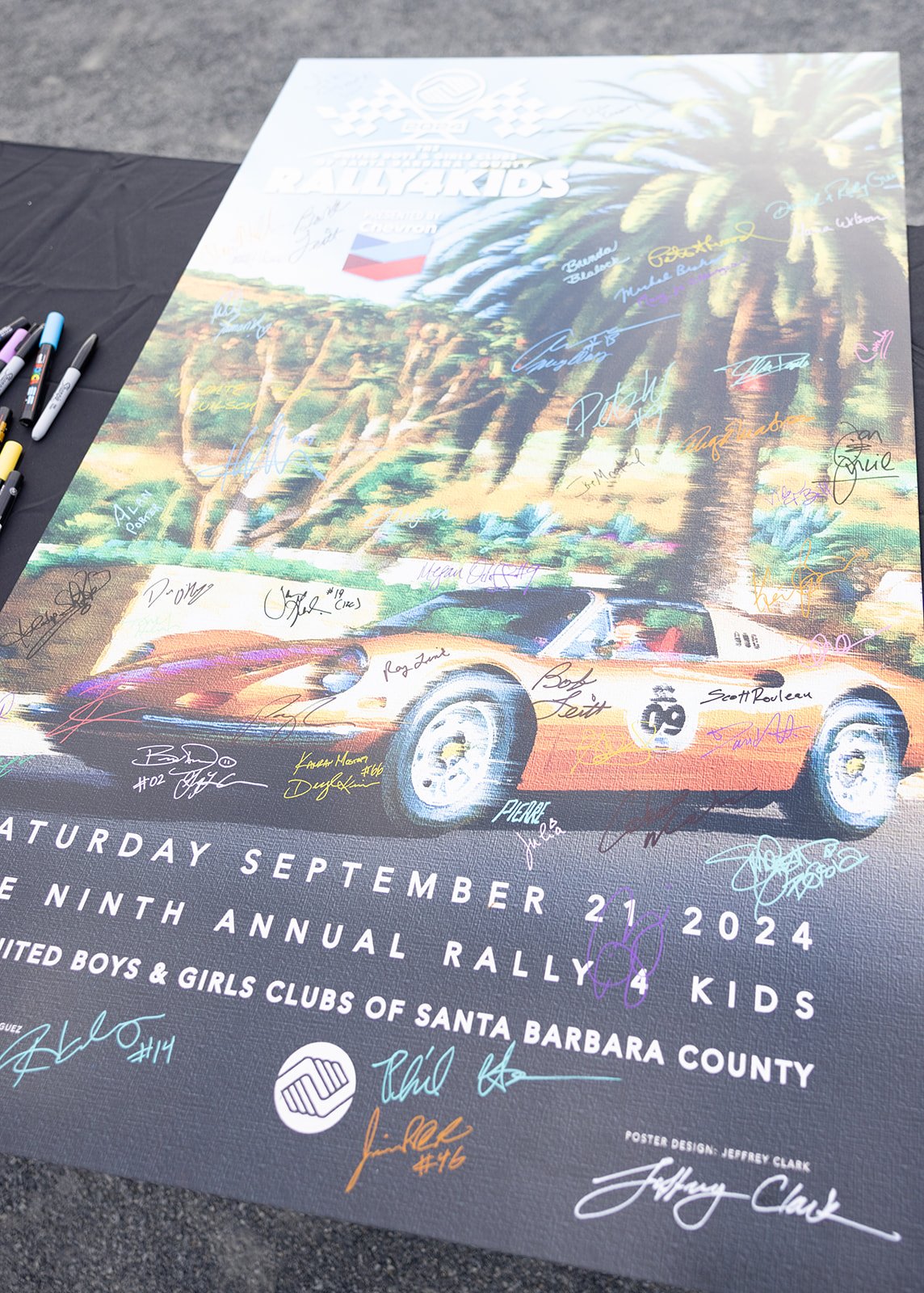 Poster for an event featuring a race car in front of palm trees with multiple signatures, celebrating the Ninth Annual Rally for Kids on September 21, 2024, organized by the United Boys & Girls Clubs of Santa Barbara County.