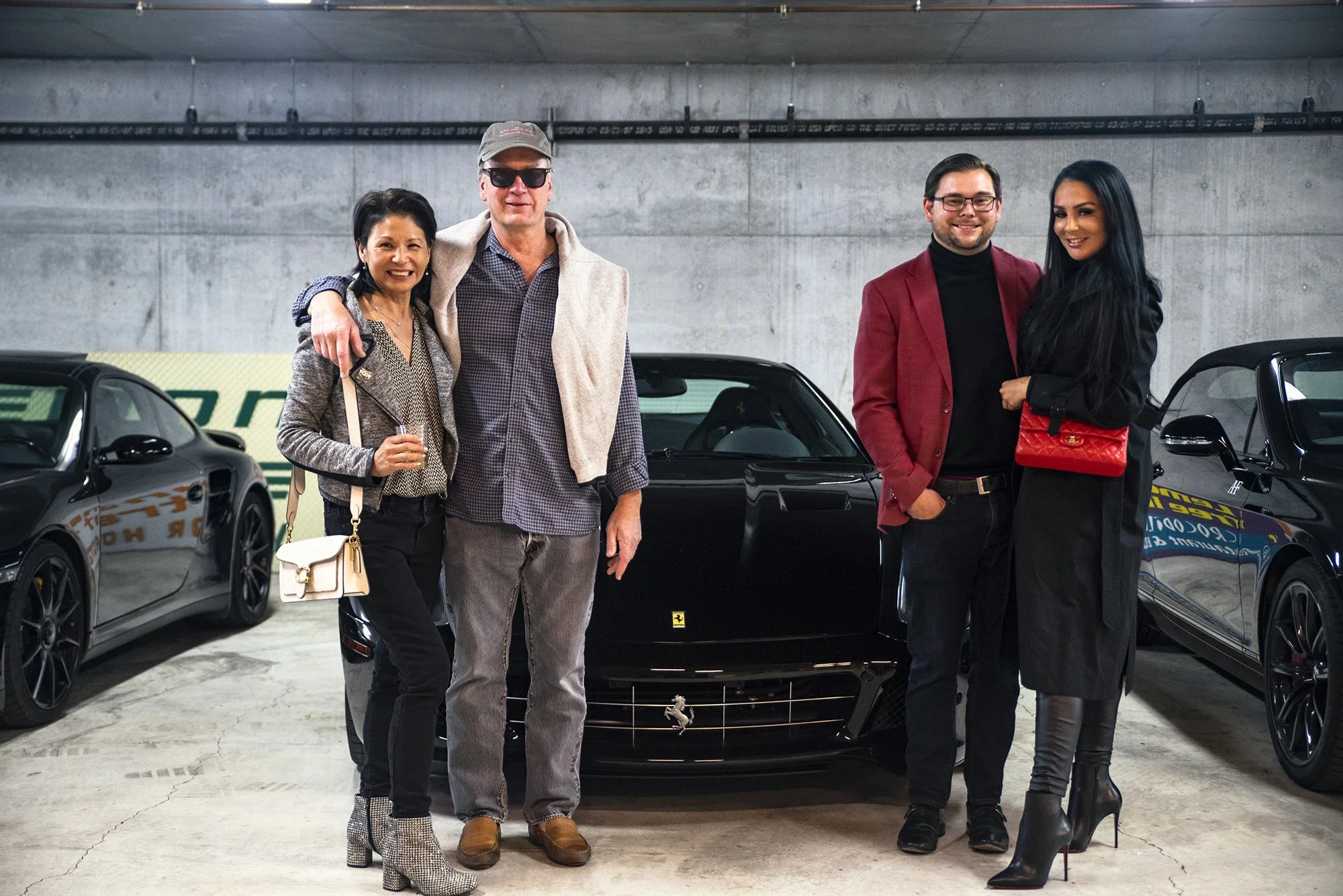 Four people standing in a parking garage in front of two black luxury cars, smiling and posing for the photo.