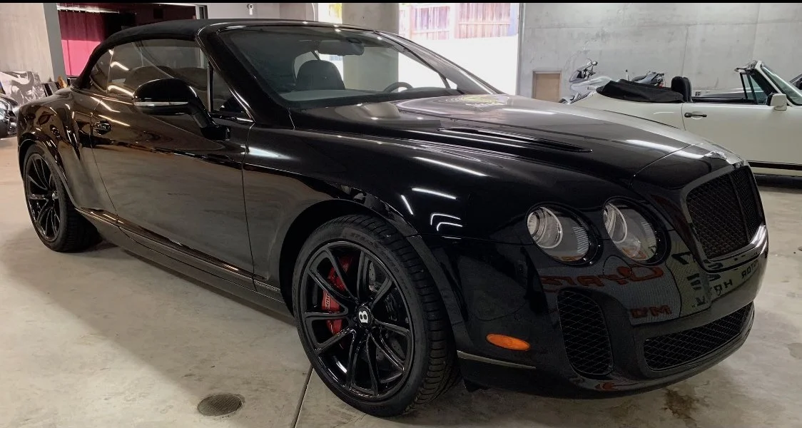 A black luxury convertible car parked inside a garage, with other cars visible in the background.