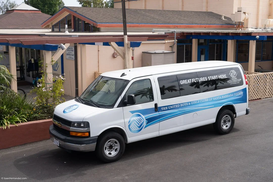 A white van parked on a street with the logo of the United Boys & Girls Clubs of Santa Barbara County, California, on the door and slogan 'Great Futures Start Here' on the side.