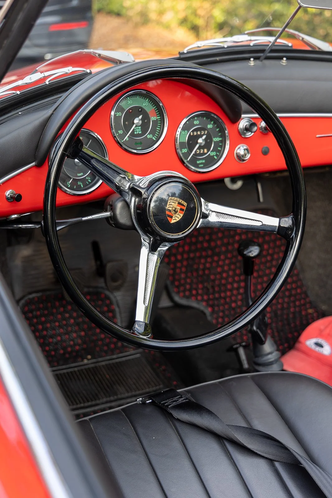 Interior of a classic Porsche with a black steering wheel, dashboard gauges, and a red interior.