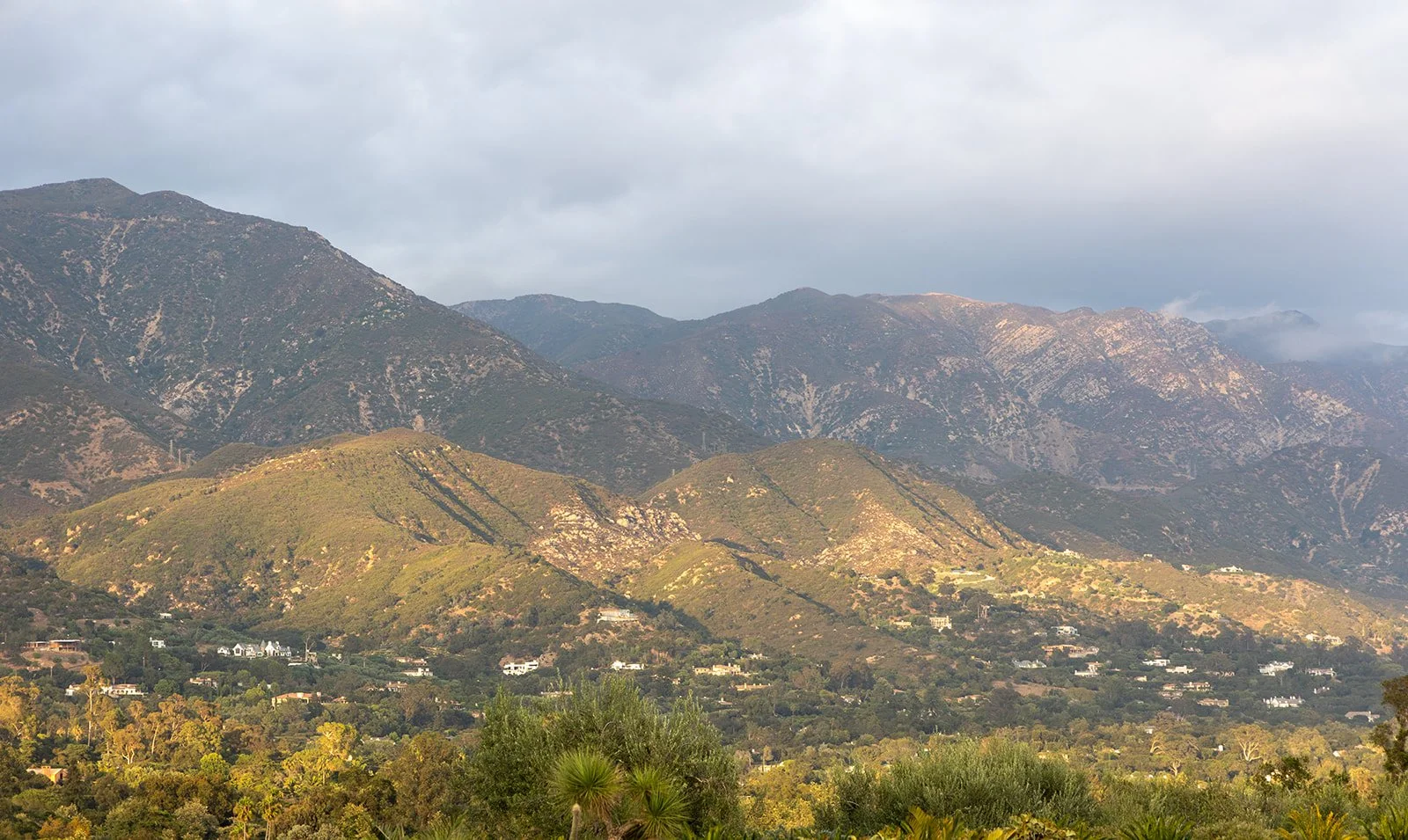 Scenic mountain landscape with rolling green hills in the foreground and rugged mountains in the background, under a cloudy sky.