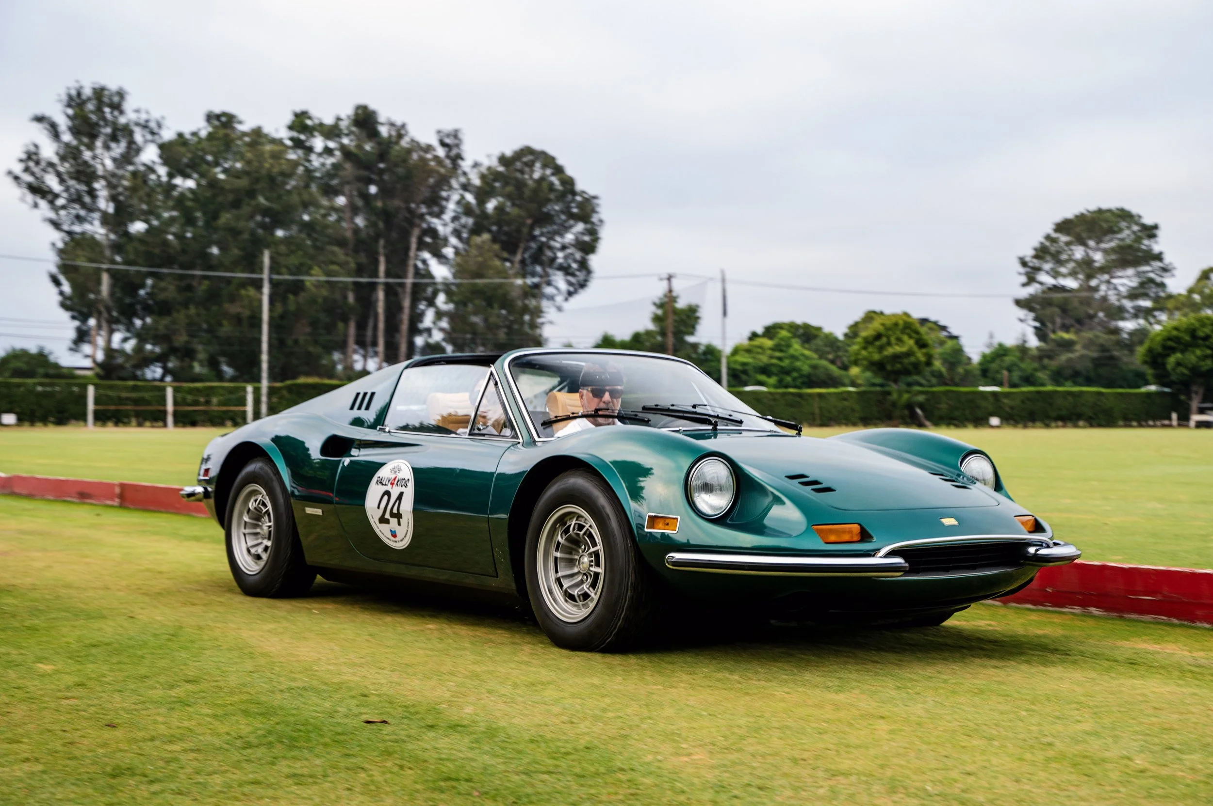Green vintage car with racing sticker number 24 on the side driving on a grassy field