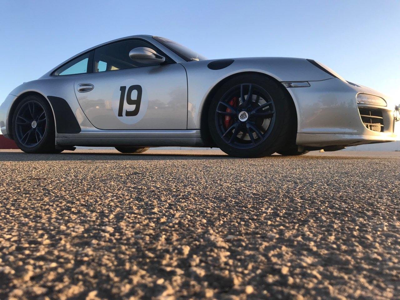 A silver race car with the number 19 on the side parked on a textured road under a clear sky.