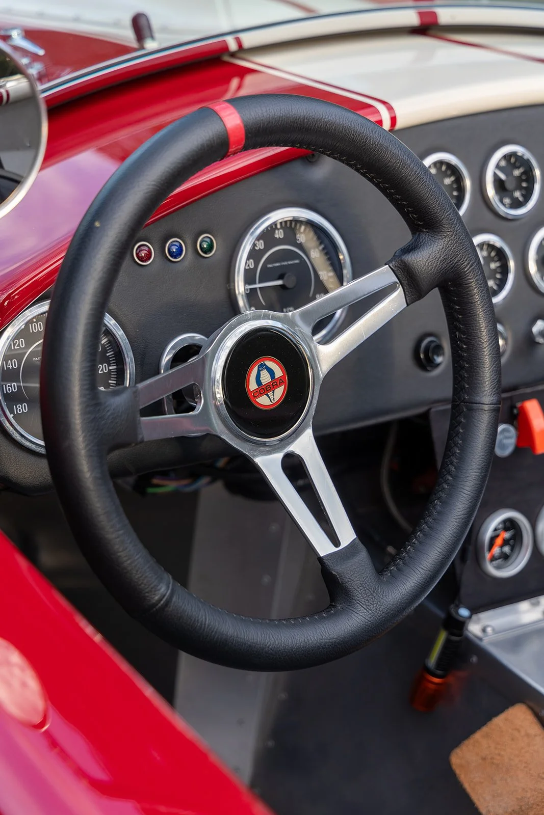 Close-up of the dashboard and steering wheel of a vintage race car, featuring the Cobra emblem at the center of the steering wheel.