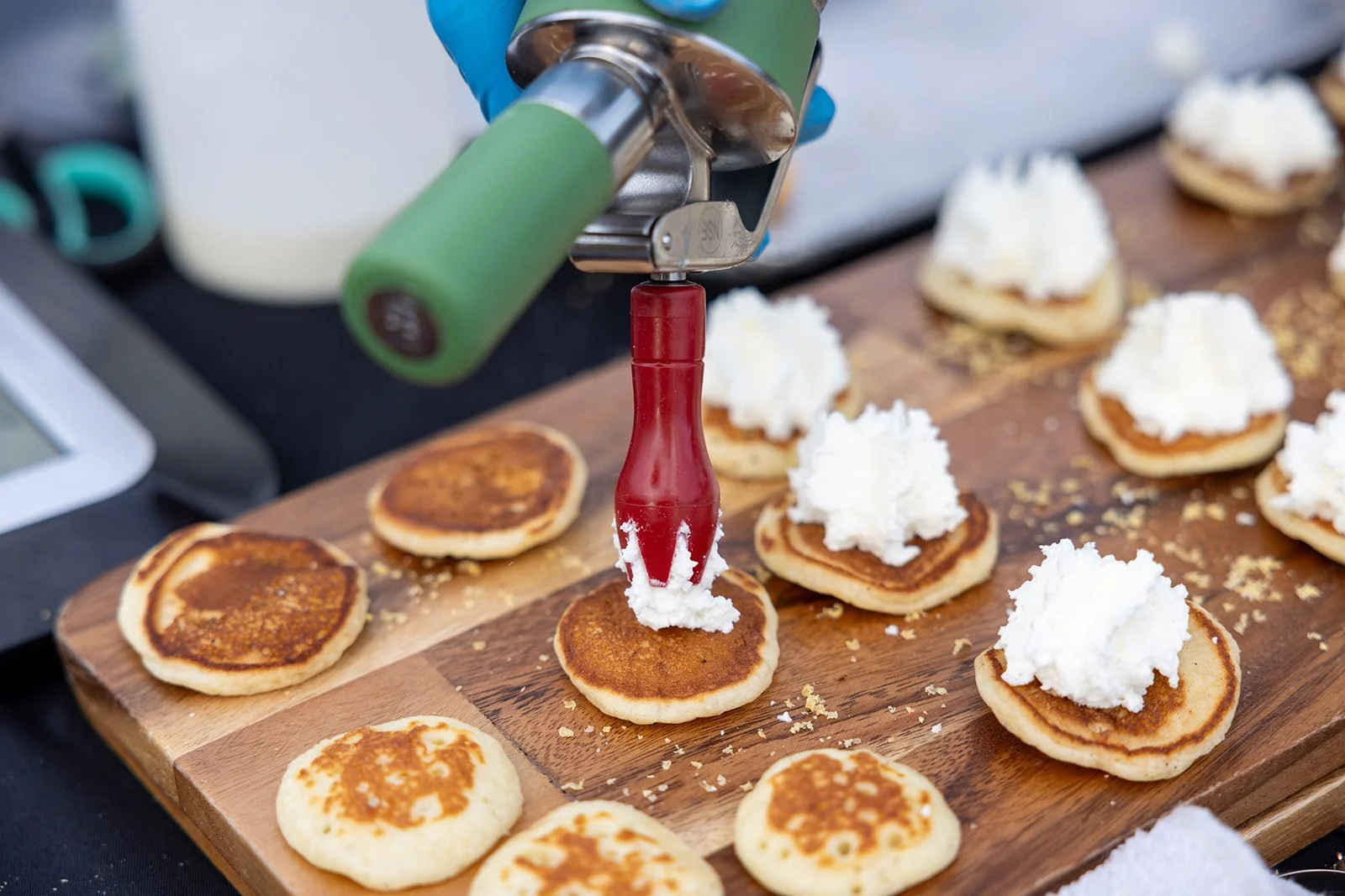 Pancakes being decorated with whipped cream using a piping tool on a wooden board.