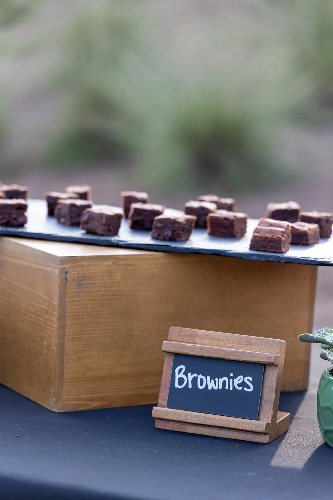 Small chocolate brownies on a slate tray at a table with a small chalkboard sign labeled 'Brownies'